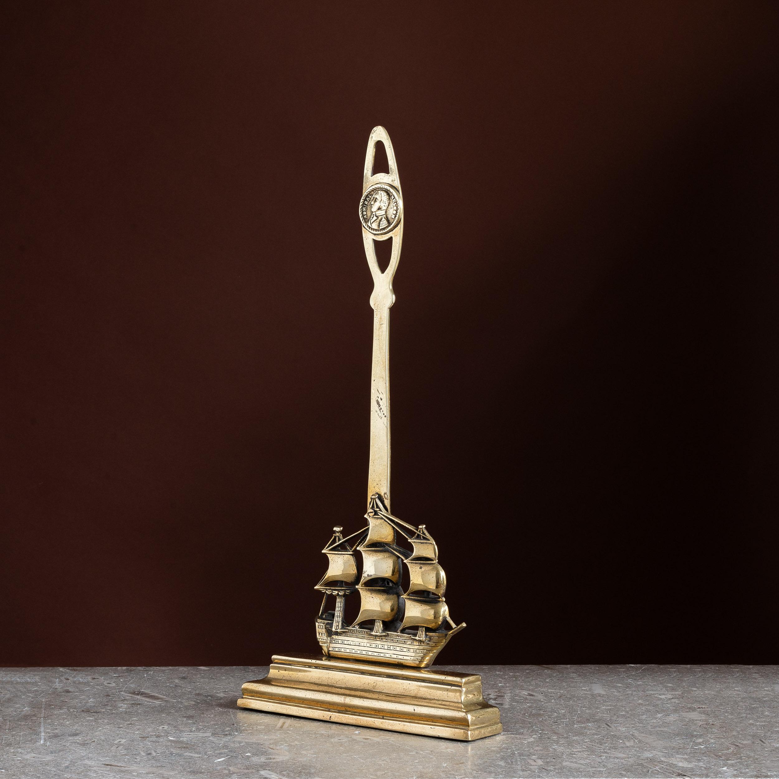 Una porta vittoriana in ottone della HMS Victory, con medaglione raffigurante Lord Horatio Nelson sulla maniglia, l'ammiraglia posta su un basamento a gradini, con pesi in piombo sul retro.