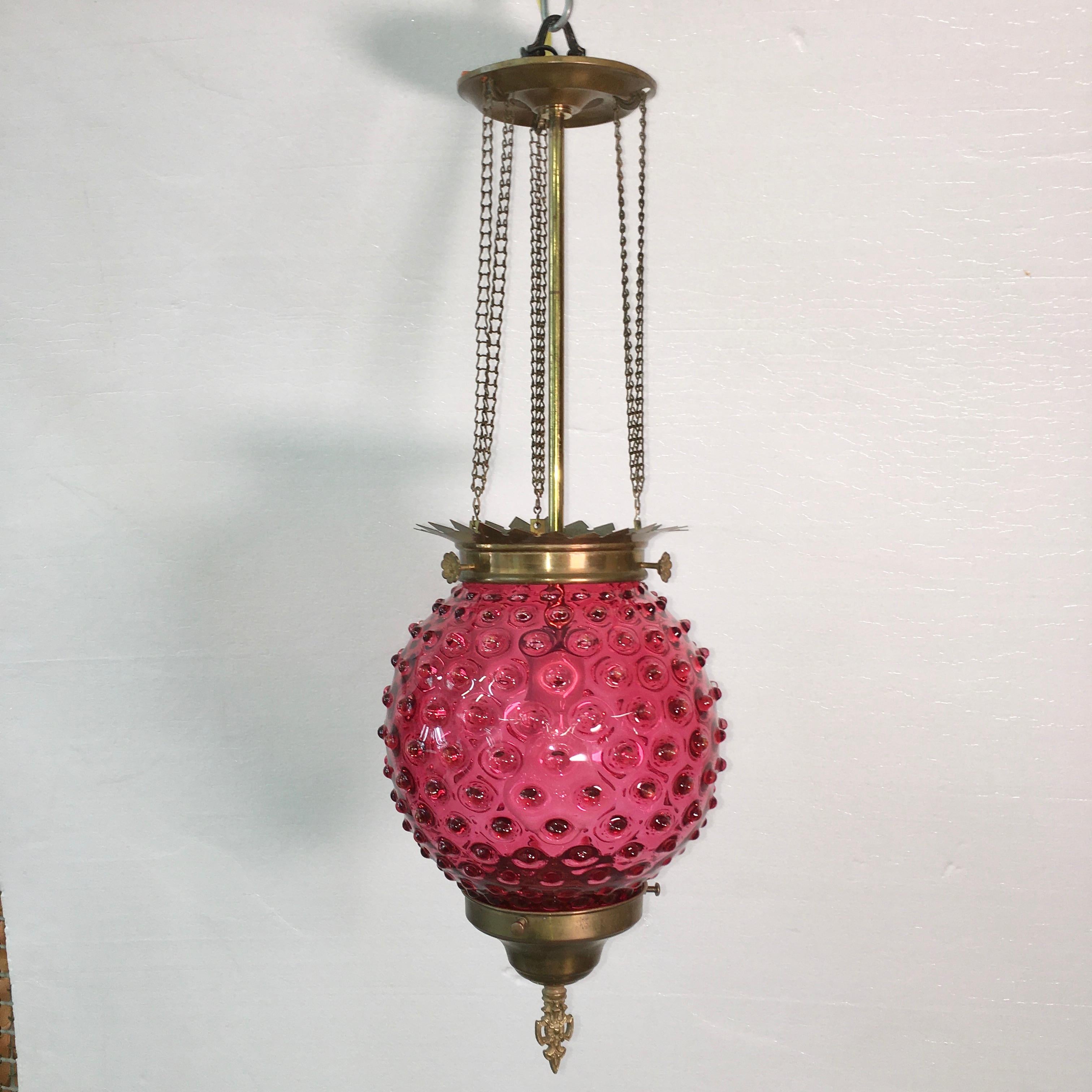 Antique electrified kerosene lantern pendant with hobnail motif cranberry glass globe suspended from brass chain. Takes a single standard Edison screw E27 lightbulb up to 100 watts. Rewired. Ready to install.