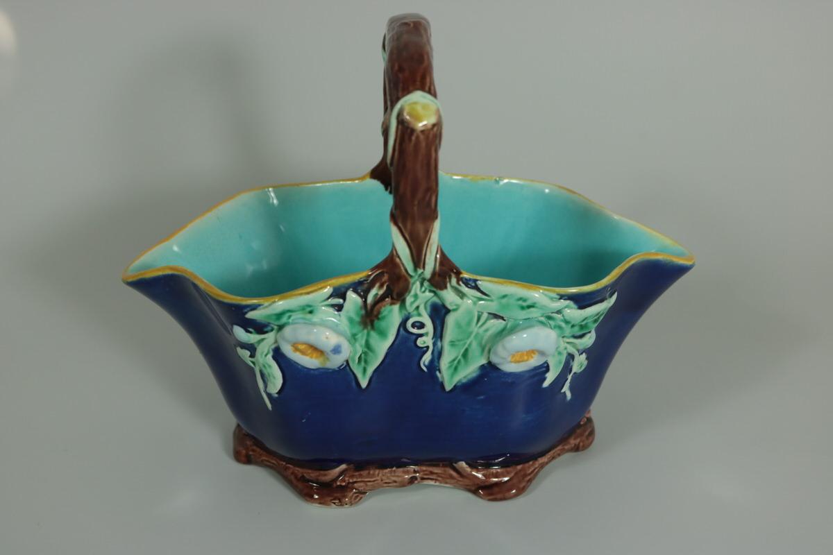 Holdcroft Majolica basket which features flowers and leaves hanging from the branch-like handle. Coloration: cobalt blue, turquoise, brown, are predominant. The piece bears maker's marks for the Holdcroft Pottery.