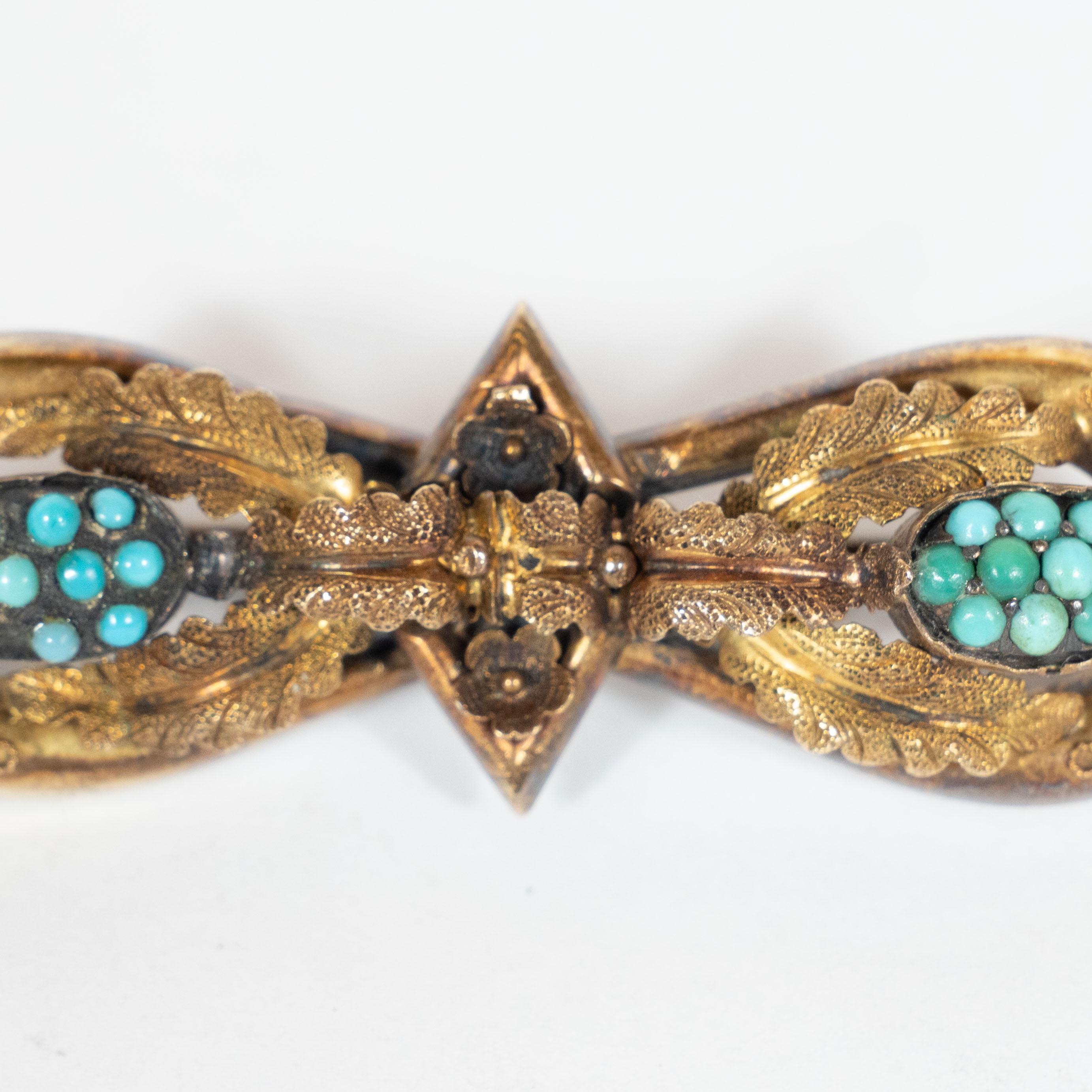 This elegant victorian brooch was realized in the United States, circa 1920. it features two ovoids that together create an hourglass shape that meet in the center at a diamond form. A collection of circular turquoise stones sit in in the center of