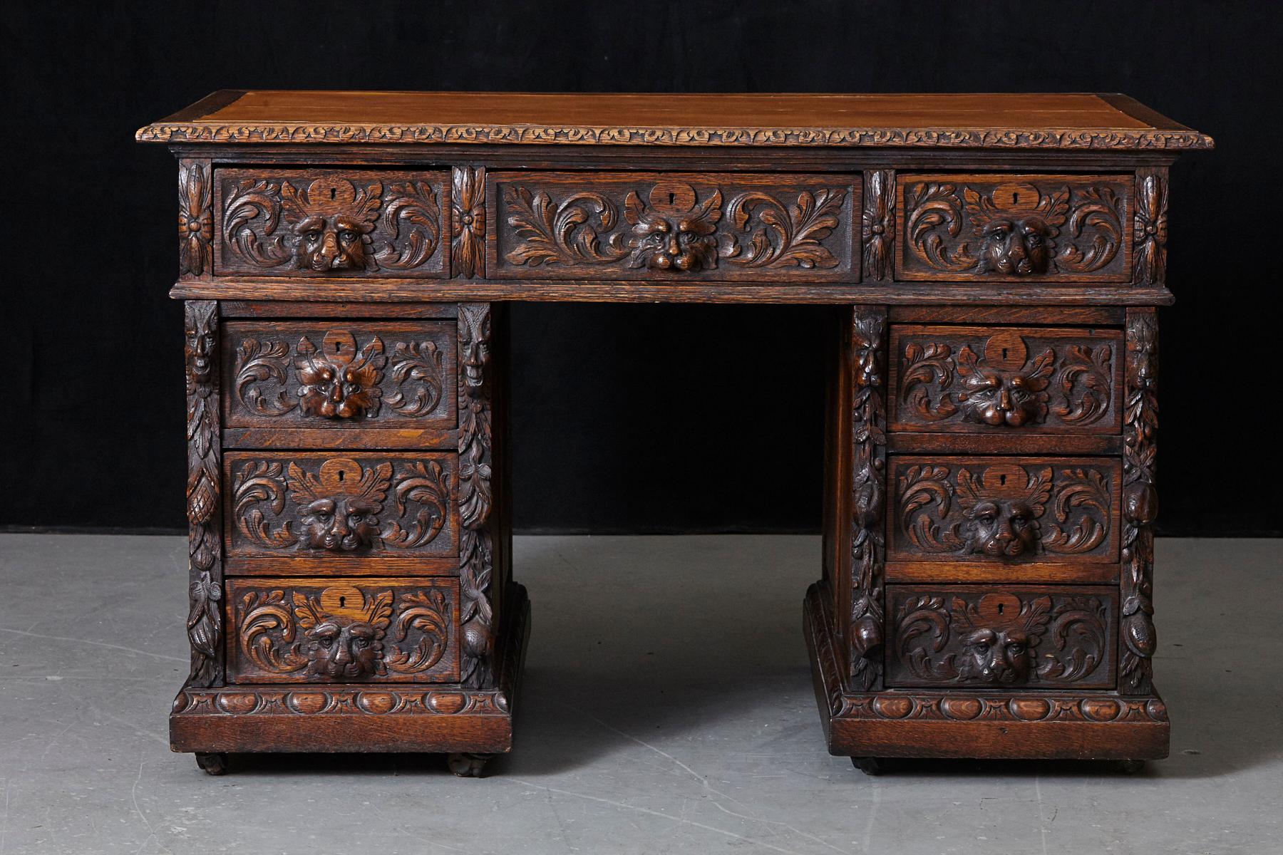 Victorian intricately carved oak freestanding kneehole desk on casters, with one long middle drawer and four graduating drawers on either side with Gothic style lion head handles.
The top of the desk has a brown replacement leather insert and the