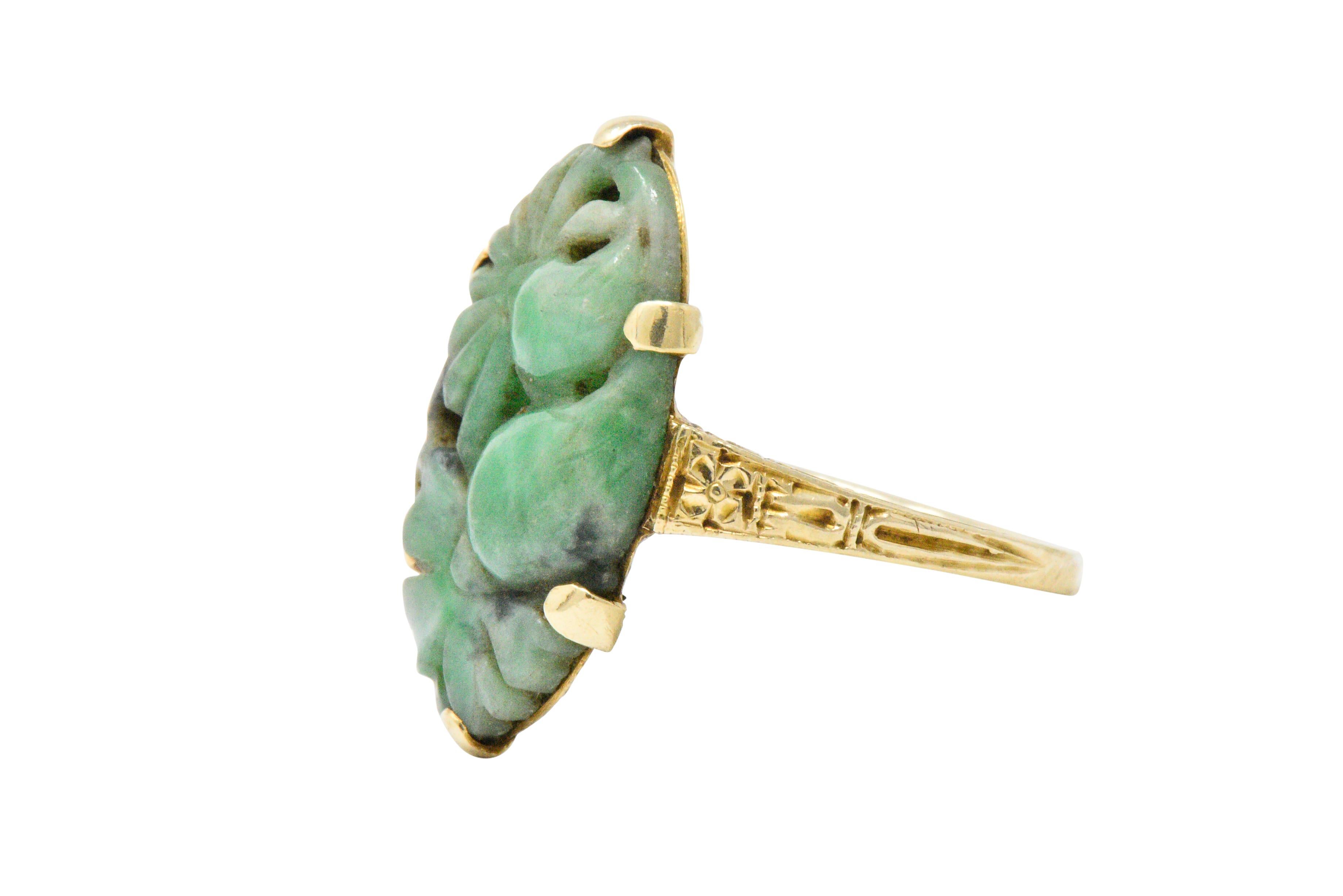 Centering a mottled green oval jade with foliate motif carving

Prong set with intricate hand engraved gold under the jade and part-way. does the shank

The ring is stamped 