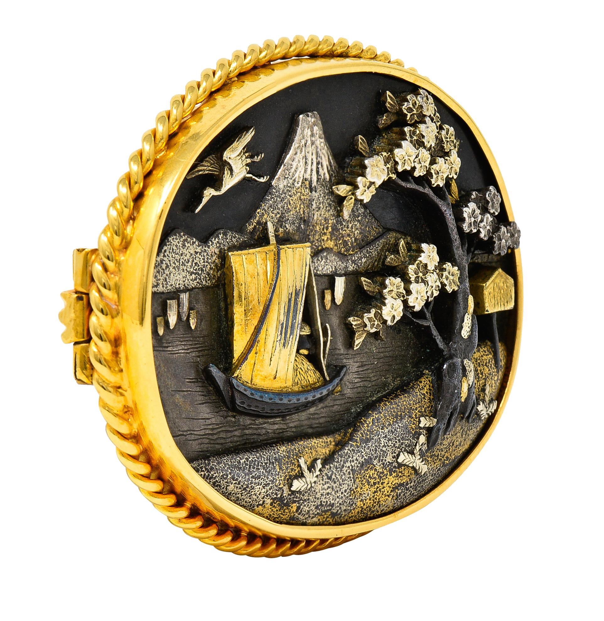 Designed as an oval shaped form decorated with a raised cameo of Japanese scenery
Depicting a cherry blossom tree, birdhouse, Mt.Fuji, sailboat, and soaring crane
Engraved and grooved with texture throughout - Shakudo style 
Comprised of oxidized