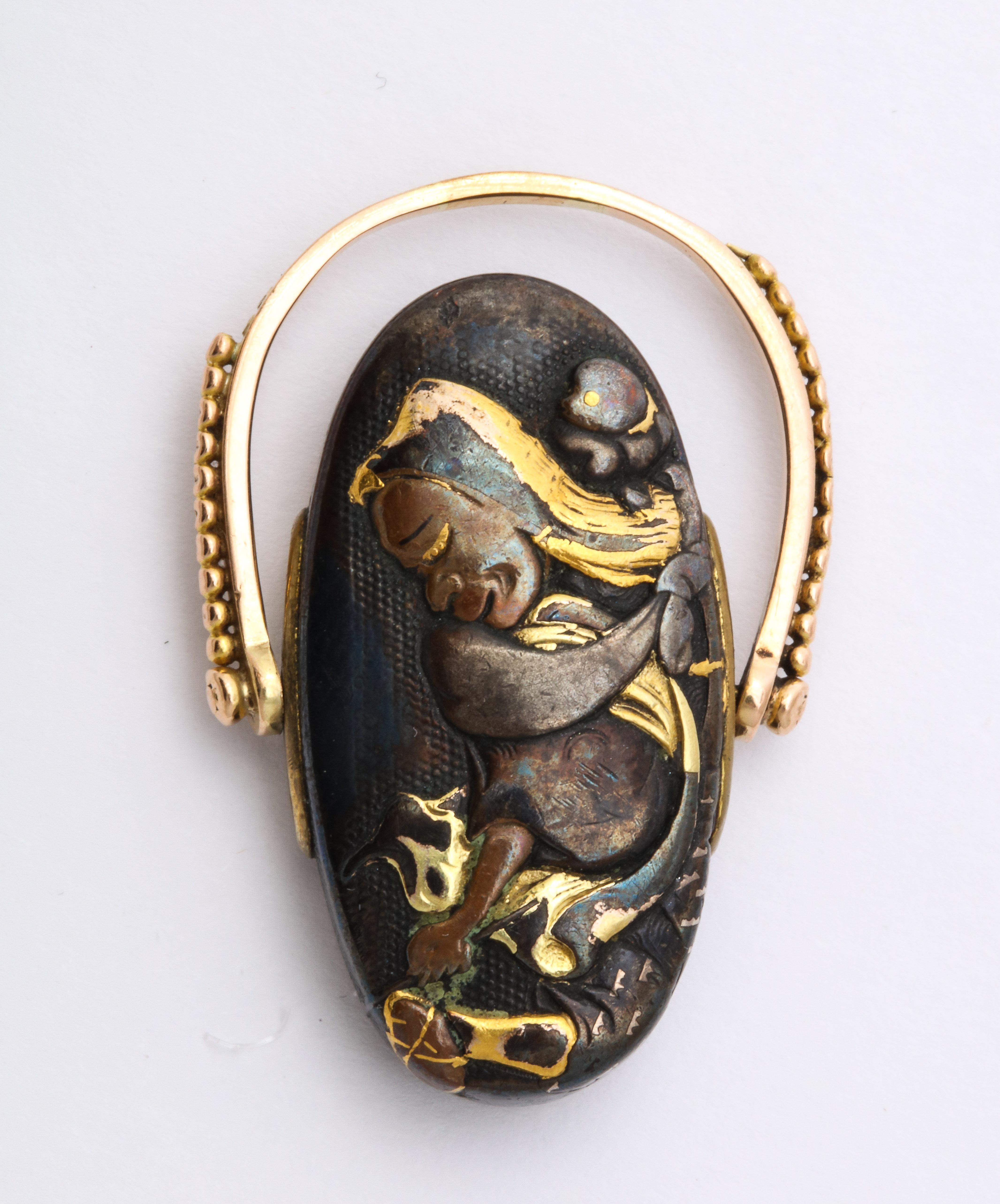 A puppy is wrapped in a golden sash on the back of a kneeling woman on this Shakudo ring c. 1870. It appears that the woman is uncovering a bone from the earth. The sash swirls through the ring like a dance. The reverse of the turning ring is a gold
