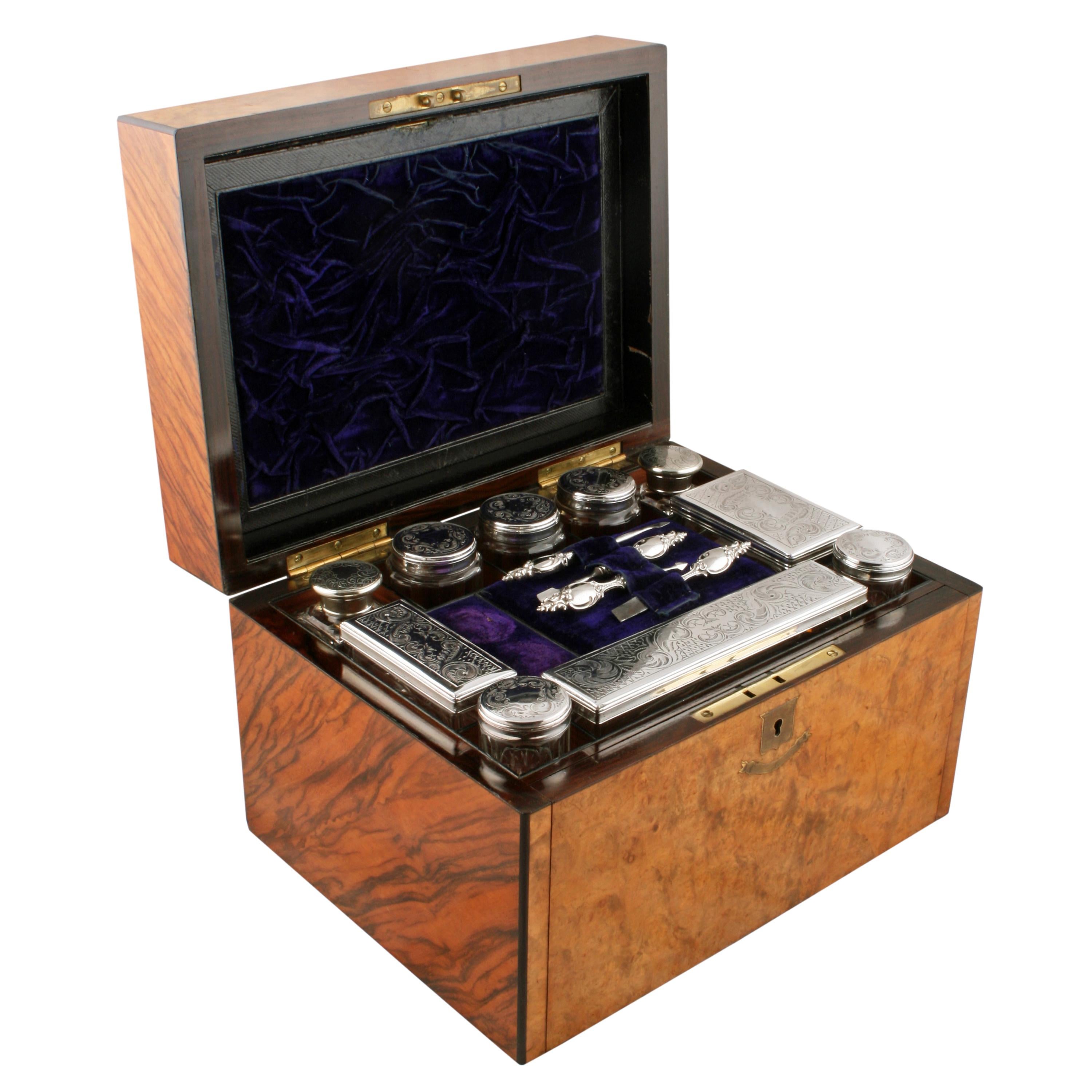 A 19th century Victorian burr walnut jewelry and dressing box.

The box has a hinged lid, a fitted interior and a front panel behind which are a pair of drawers.

The interior holds ten glass perfume and storage jars and bottles with silver
