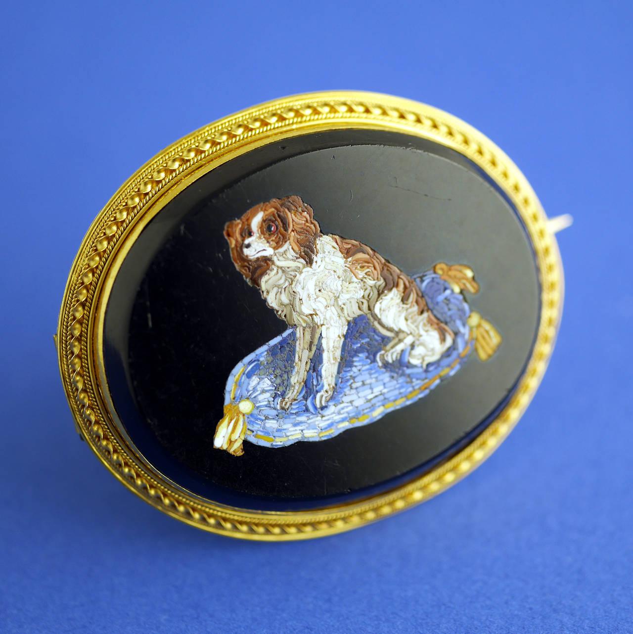 Feines Mikromosaik, das einen King-Charles-Spaniel-Hund auf seinem Kissen darstellt, gefasst als Brosche in 18 Karat Gold. 

Hunde waren ein Symbol für treue Liebe. Die King-Charles-Spaniel-Rasse war bei der englischen Aristokratie äußerst beliebt,