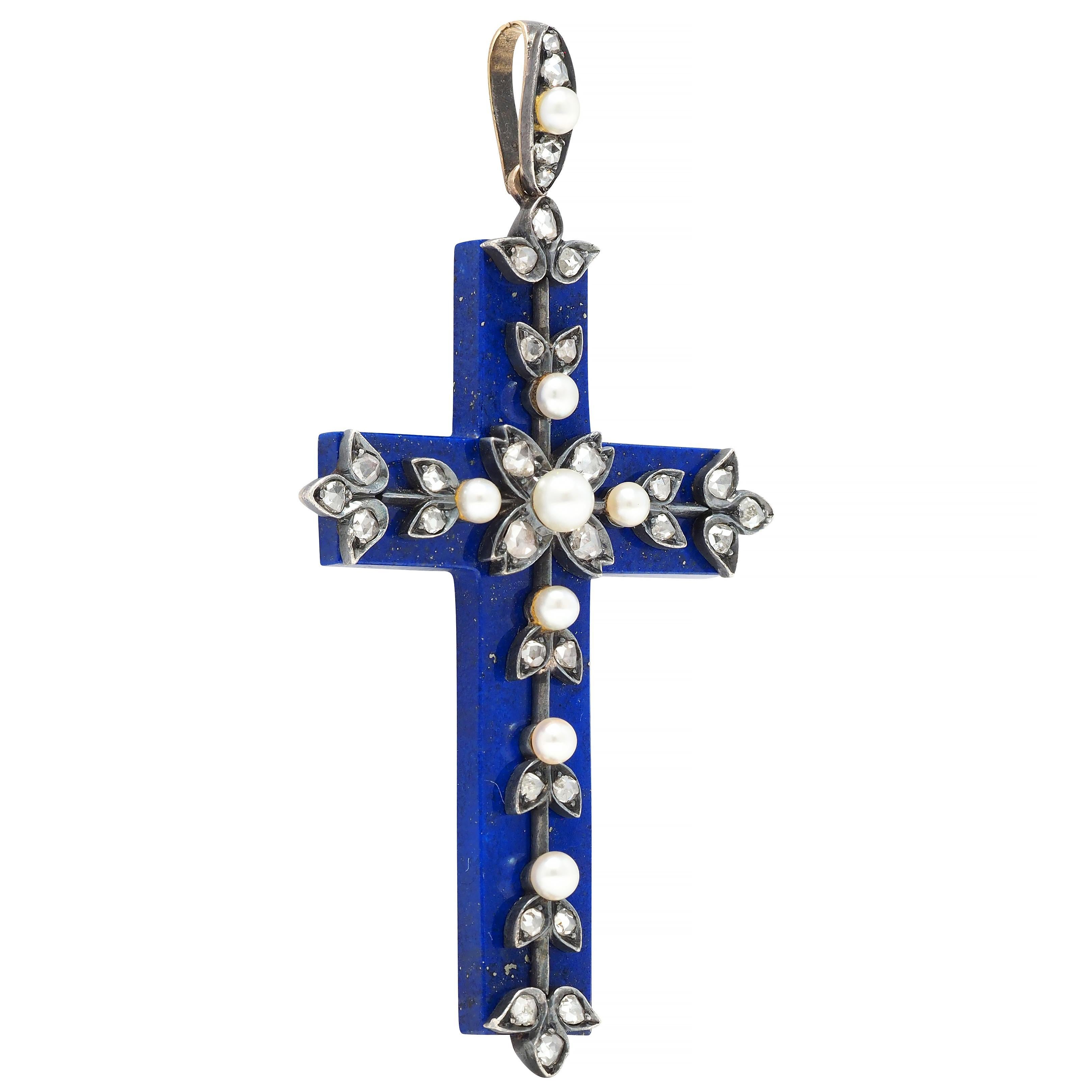 Designed as a marquise shape surmount suspending a cross pendant of carved lapis lazuli 
Opaque ultramarine blue with gold pyrite flecking and decorated with vine motif appliqué 
Silver-topped and bead set with approximately 1.48 carats of rose cut