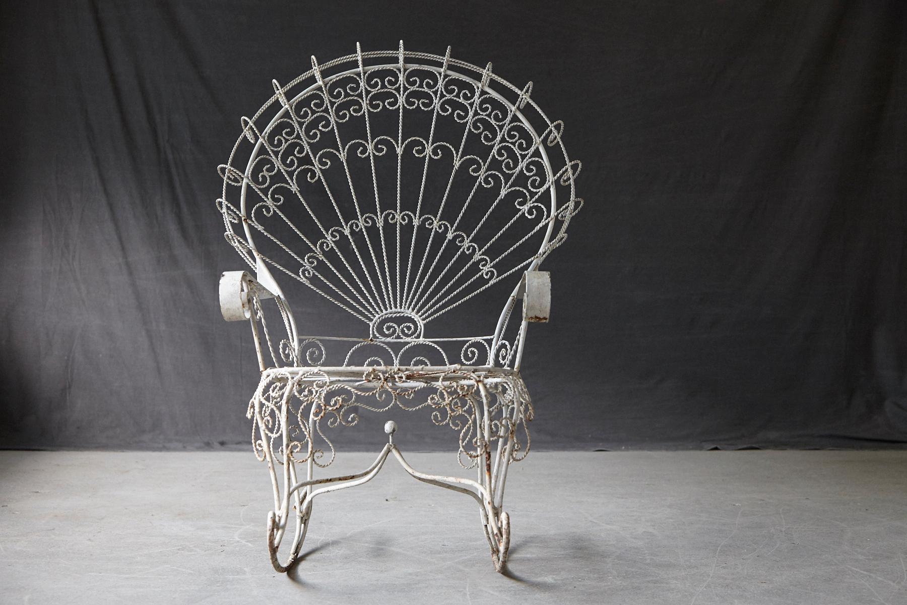 Lovely John Salterini mid-century modern lawn furnishing wrought iron peacock rocking chair, with lacy wirework, a wrought iron frame resembling a peacock's fanned tail. 
Sturdy piece with fading and chipping paint and some oxidation to the base,