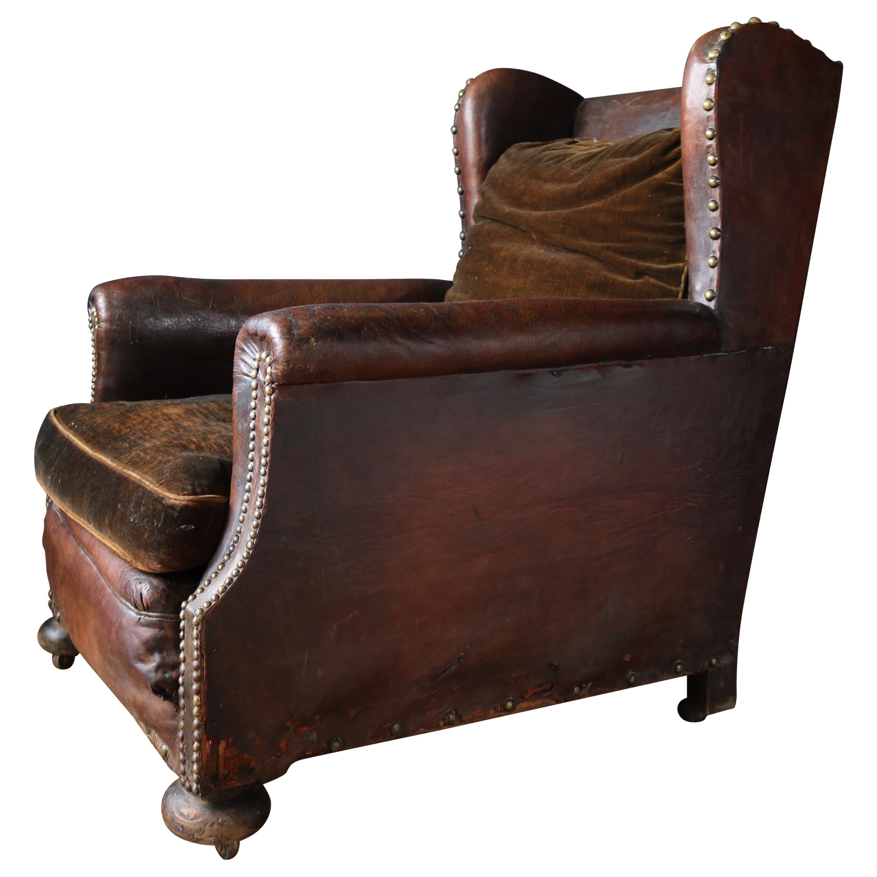 A wonderful late 19th century leather wingback club chair, fantastic color and patina throughout with large brass studs the chair comes with three brown velvet cushions, standing on oak bun feet with castors.
