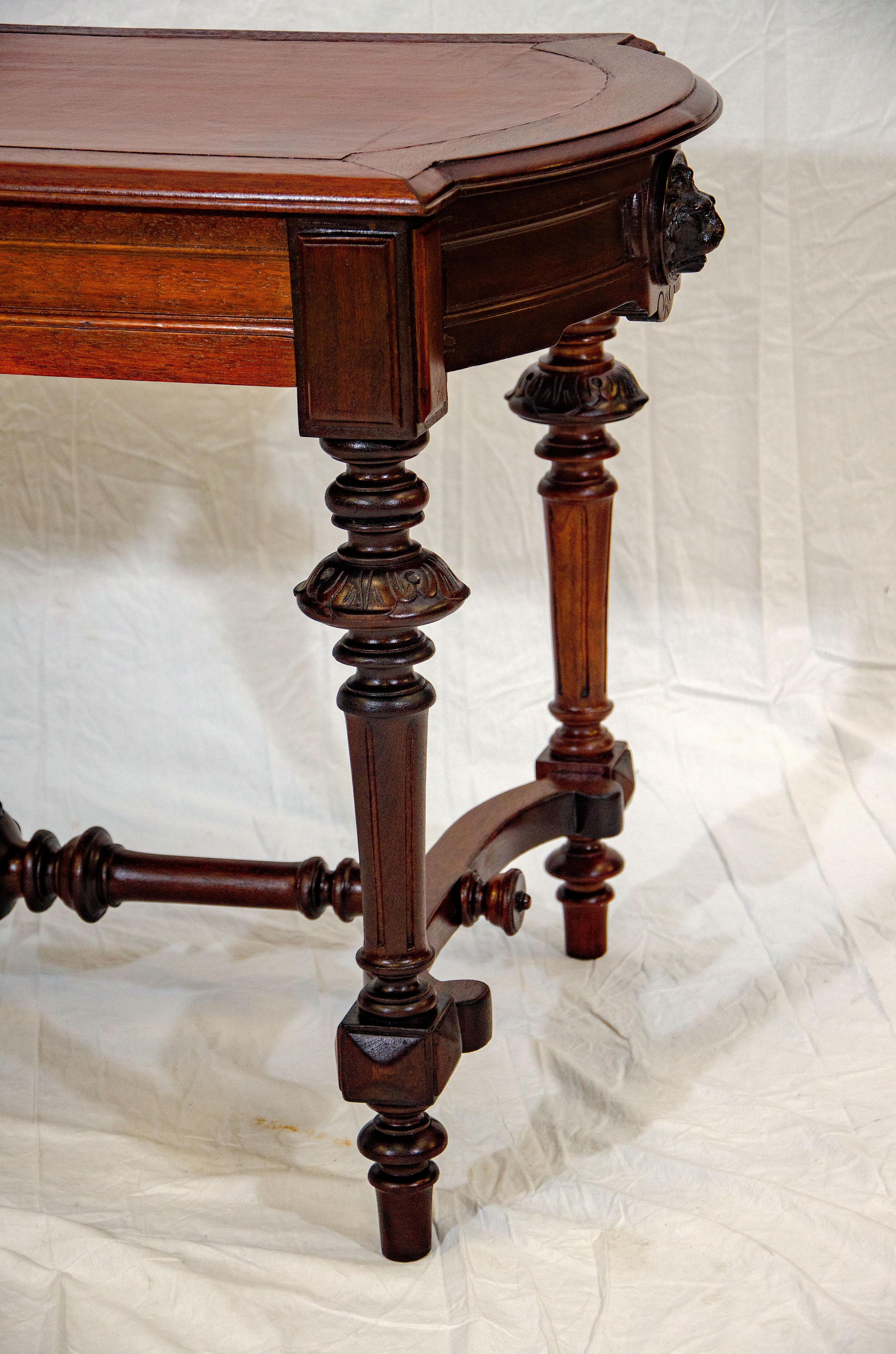 Multi-purpose victorian walnut table with leather inset. The top surface has straight sides and rounded ends. There are four turned and carved legs and carved stretchers. A lion's head inset accents the aprons at the curved ends. There is one drawer