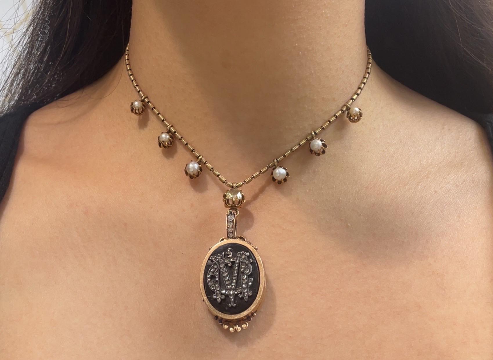 Collar relicario victoriano

Un collar medallón con una cadena adornada con seis perlas y un diamante talla rosa. El colgante presenta detalles de esmalte negro y un monograma 