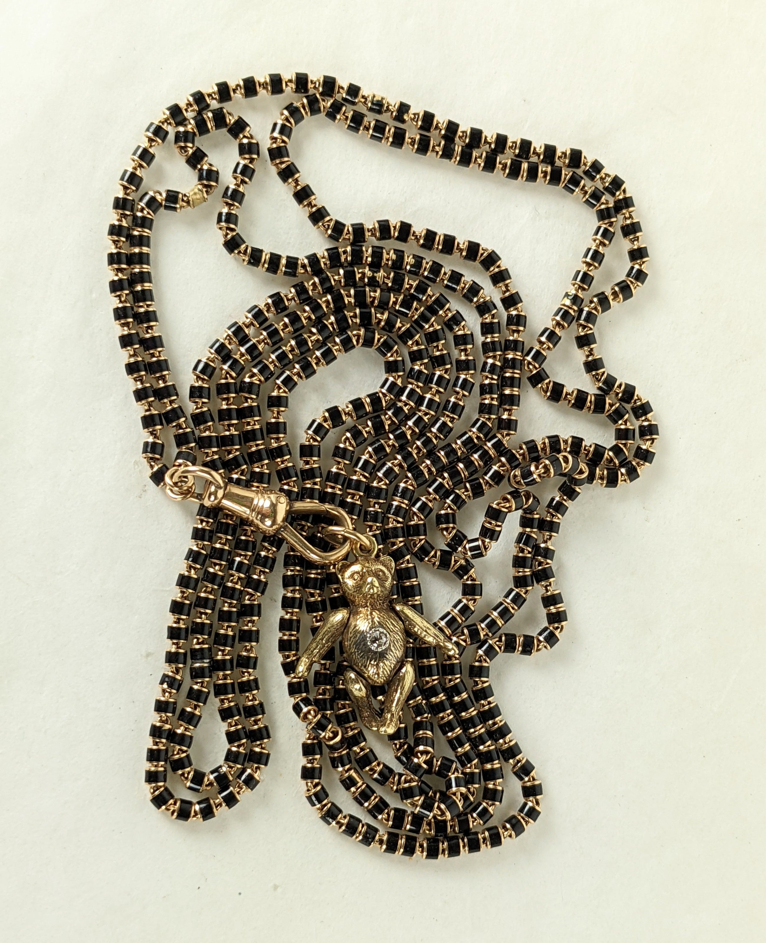 Victorian Long Chain Assemblage made of elements from the late 19th Century. A long black enamel link mourning chain in 14k from the 1880's is married to a mechanical toy teddy bear charm adorned with a single diamond from circa 1910. 
Representing