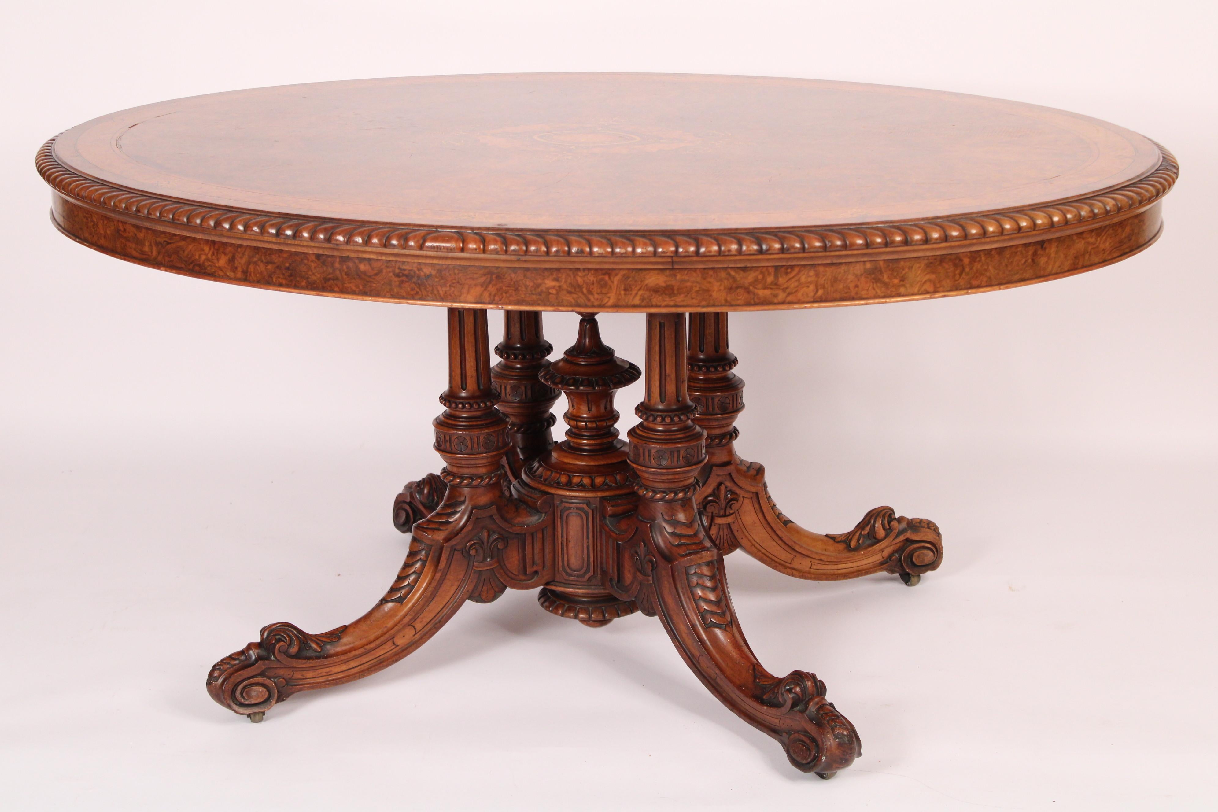 English Victorian burl walnut and carved walnut loo table, late 19th table. With an oval burl walnut inlaid top with gadrooned borders, 4 turned fluted columns attached to 4 carved down swept legs. The quality of woods and workmanship that went into