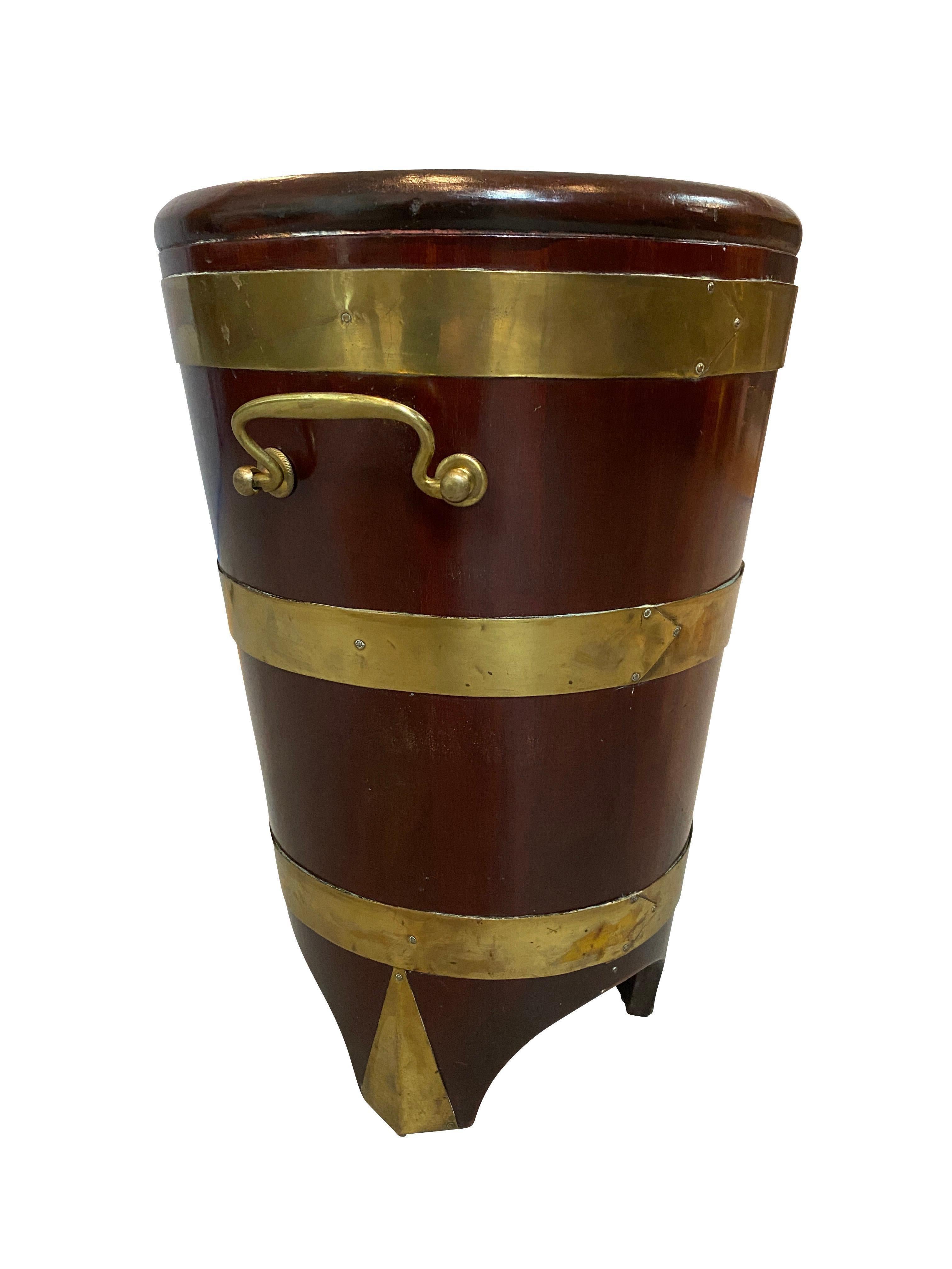 Tapered cylindrical form with three brass rings ending on three bracket feet with triangular brass applied panels. Brass bail handles.