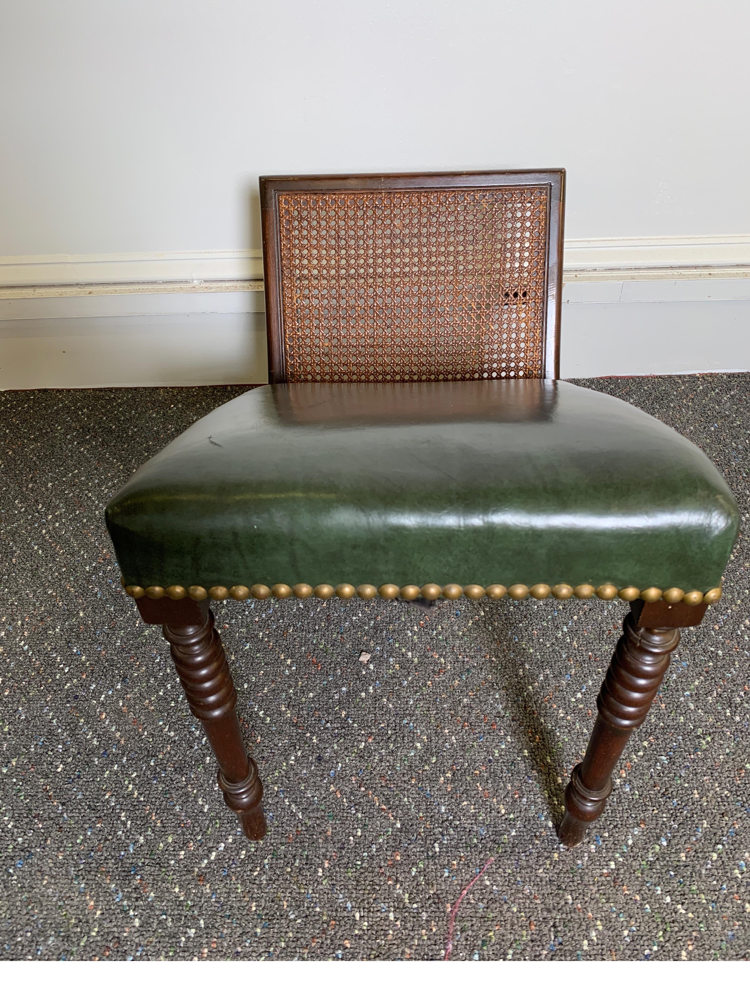 A late 19th century mahogany and leather gout stool in well cared for original condition. The Leather upholstered cushion with brass nailhead trim with a caned side with mahogany frame. Old repair on the leg.