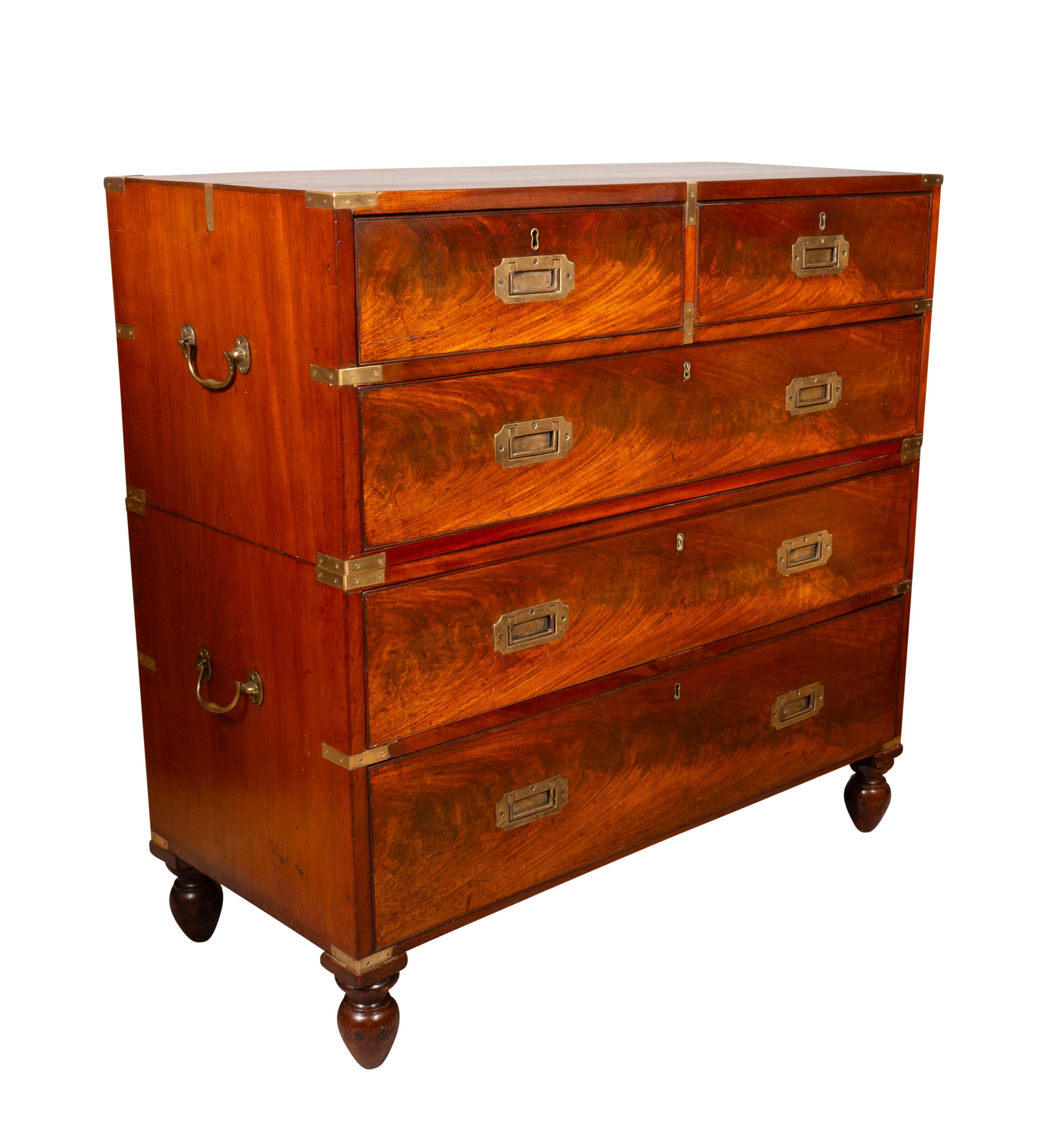 In two sections. Rectangular top with brass corners with two over three drawers. Inset brass handles and side carrying handles. Turned feet. This was possibly converted from a regular chest to a campaign chest or the handles were replaced.