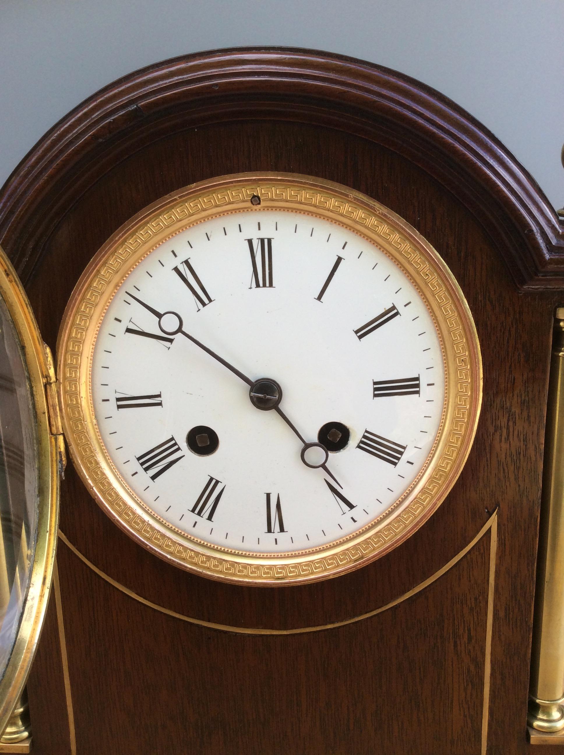 Mahogany mantel clock in a break arch case with brass columns to either side, brass inlay to the front and surmounted by four brass finials.

Beautifully decorated brass bezel, enamel dial with Roman numerals and original ‘blued’ steel