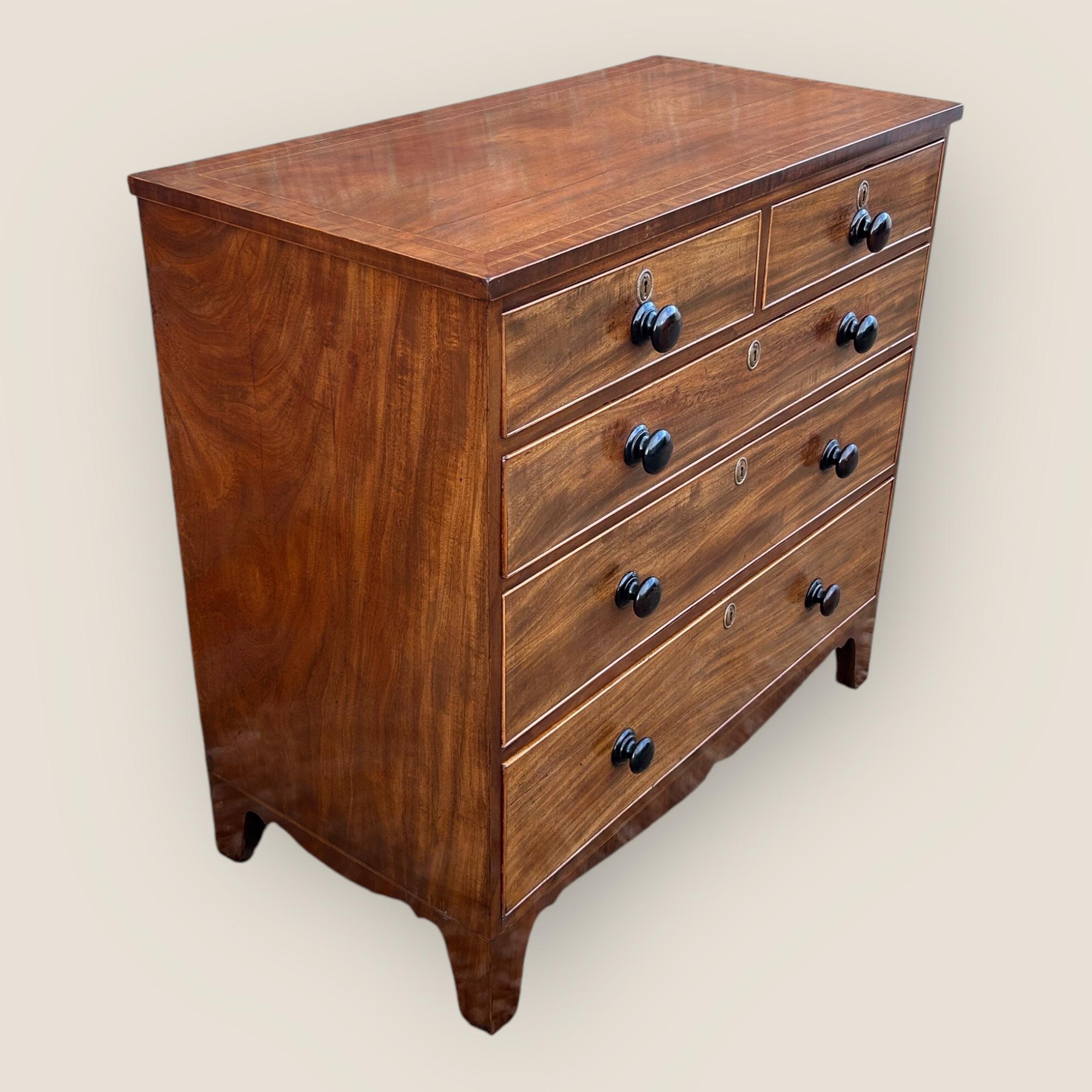 Commode en acajou du début de l'époque victorienne (vers 1837-1860), avec des poignées en bois à bouton simple, des inscriptions sur les clés en laiton et des pieds évasés. Cette commode a un plateau marqueté avec des bandes transversales et des