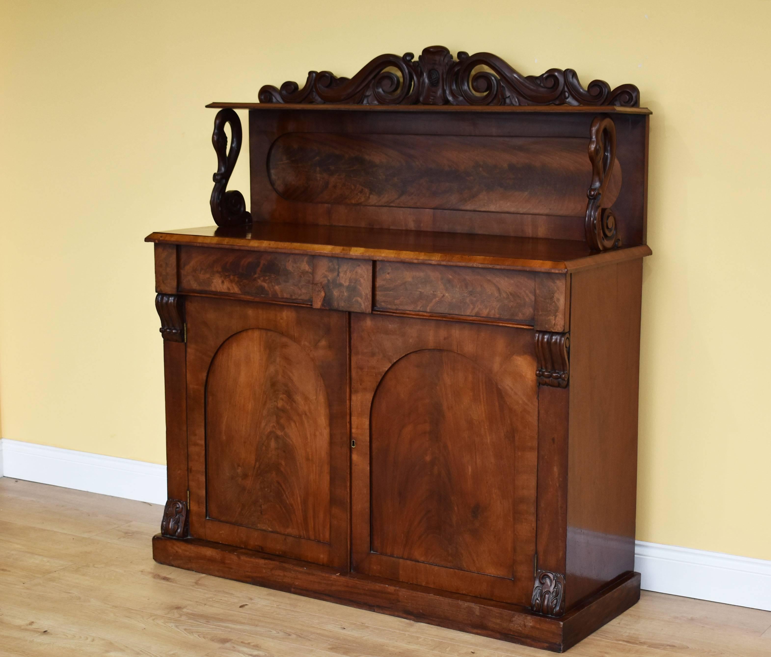 For sale is a good quality Victorian Flame Mahogany Chiffonier. The chiffonier has a single tier upstand, with two column supports in the form of swans. Below this there are two drawers above a cupboard opening to reveal a single shelf, above a