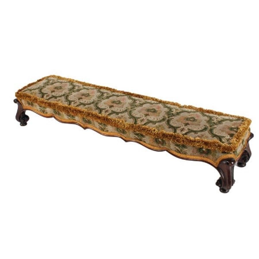 A 19th century Victorian mahogany long fender footstool.

The stool has a foot rest that is angled higher to the back, a serpentine lower edge to the front and stands on four carved scroll toe feet.

The upholstered foot rest has a half round
