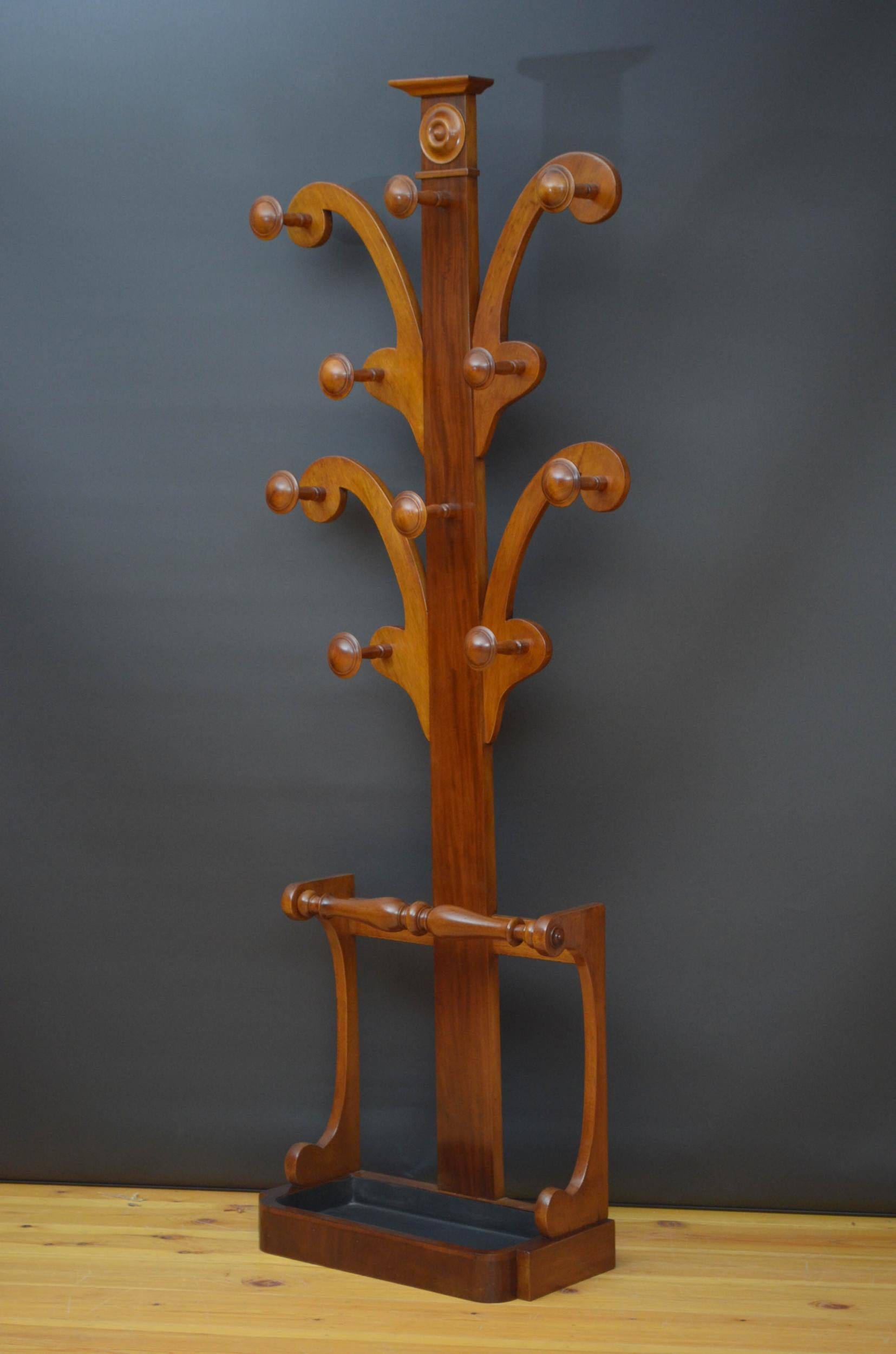 Sn4916, elegant Victorian hall tree in mahogany, having four arms with original turned coat and hat hooks on figured mahogany upright with additional hooks terminating in shaped base with carved supports and original drip tray. This antique coat