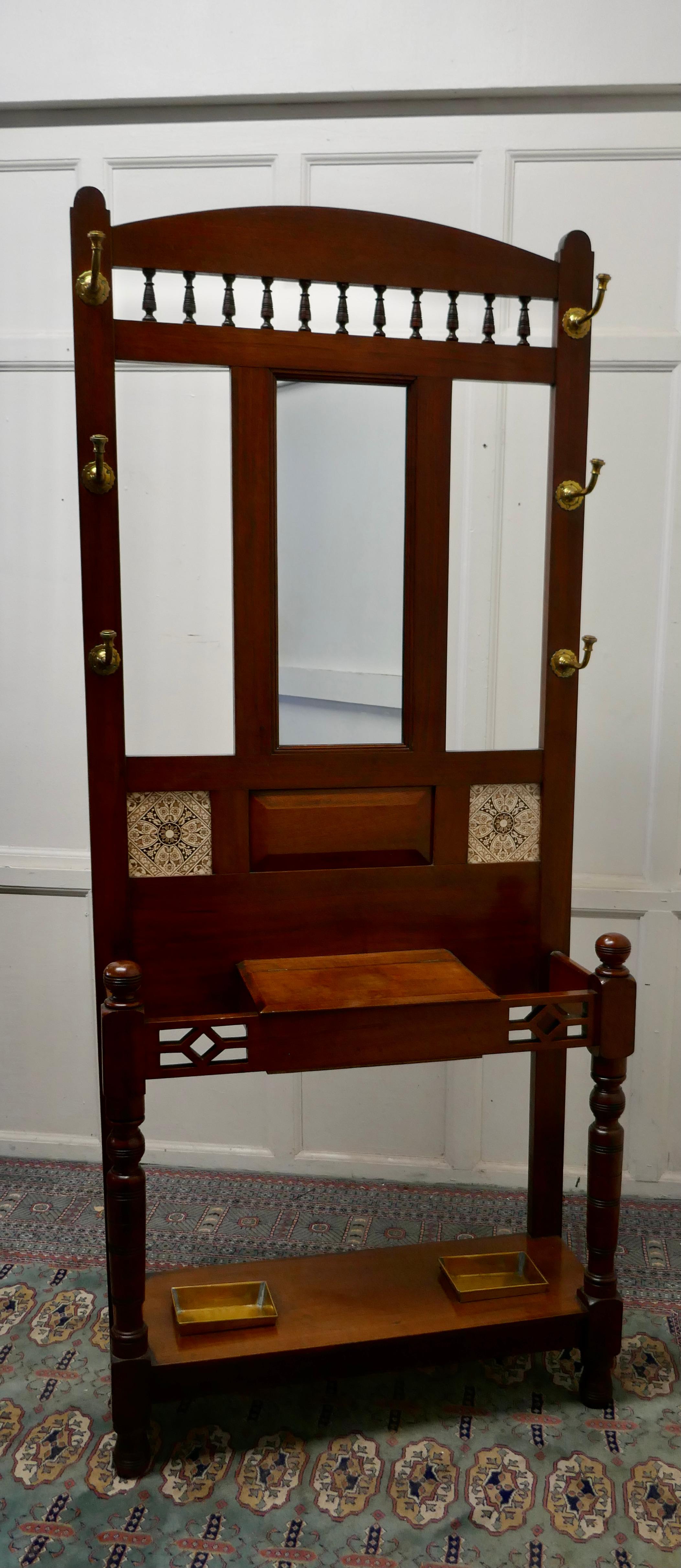 Victorian Mahogany hall stand 

This is a handsome piece, the stand has a central mirror, 6 brass coat/hat hooks and central closing glove box 

The upper section has attractive Victorian Tiles, and the lower section has brass drip trays for