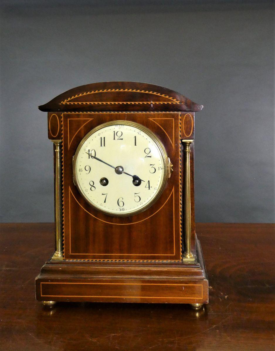 Late Victorian mahogany mantel clock in a dome top case line inlaid with satinwood stringing and bordered with chequered ebony and satinwood.

Standing on a raised plinth and resting on turned brass feet.

Turned brass pillars to either side of