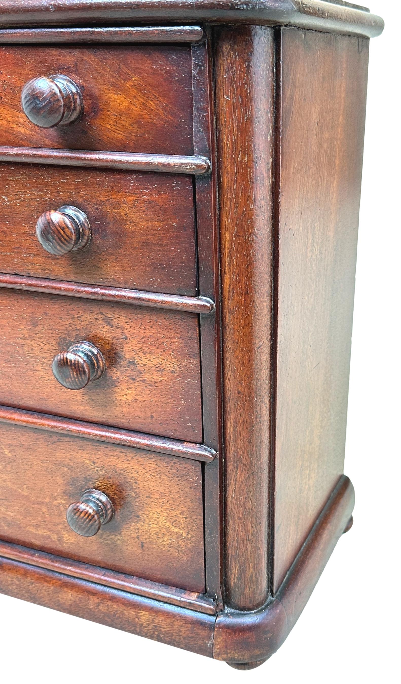 A charming late 19th century mahogany minaiture chest, having rectangular top over two short and three long drawers, retaining original turned wooden knobs, flanked by rounded corners, raised on original turned wooden feet.

Much discussion is had