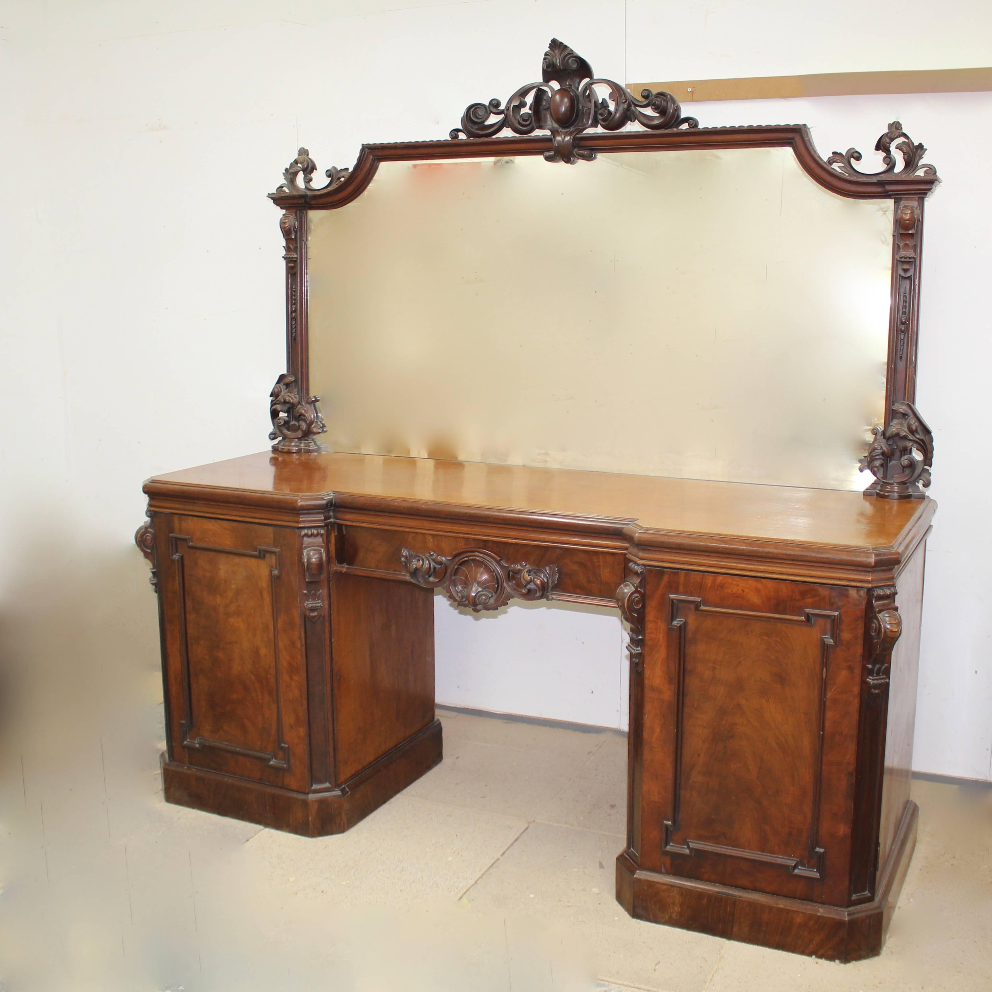 A stunning Victorian mahogany mirrored sideboard. Having a large carved mirror with central cartouche crest and flanked by decorative columns with floral and corbel decoration. The top with canted corners stands above a nicely carved central drawer.