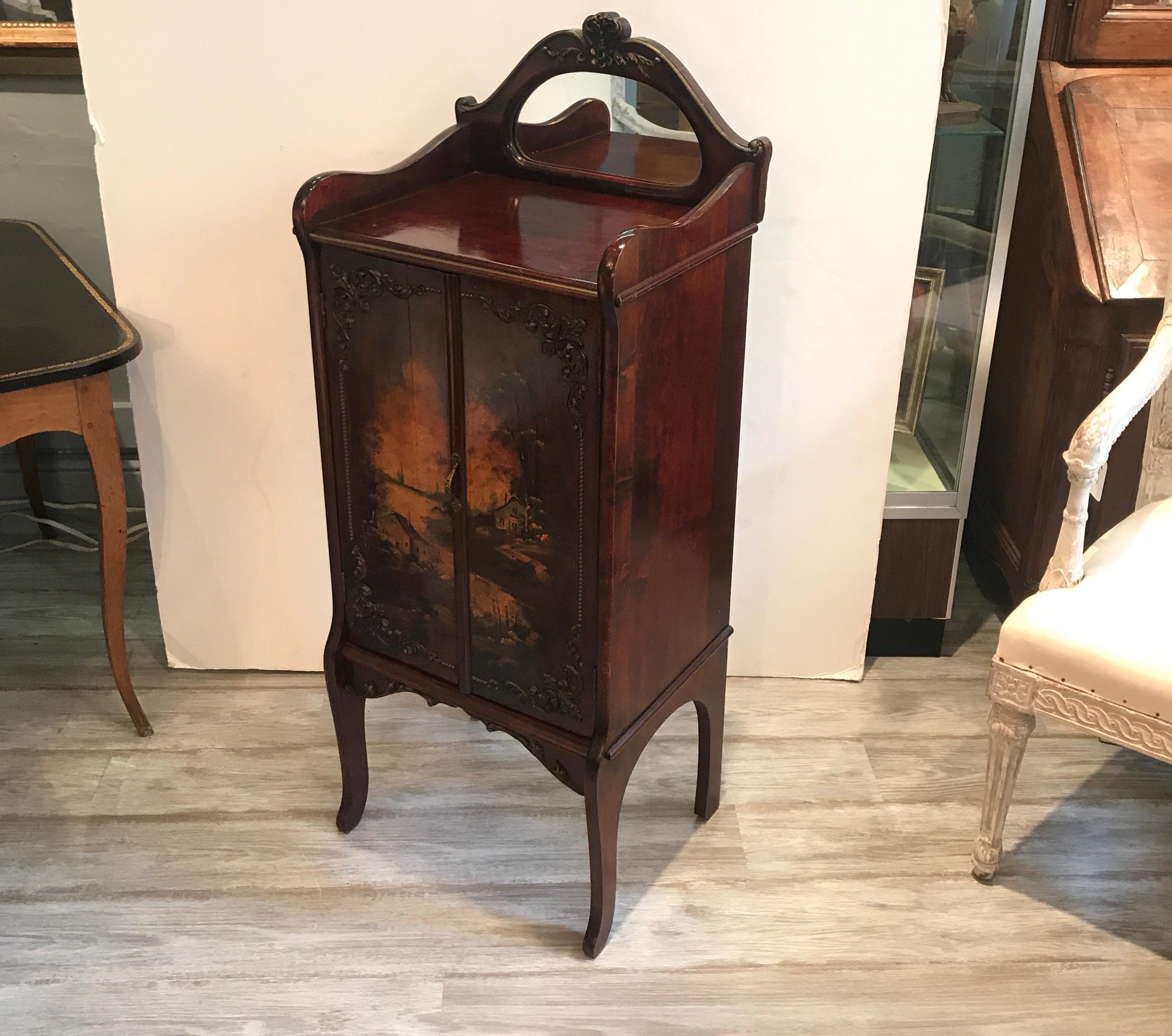 Solid mahogany music cabinet stand with hand painted decoration. The front doors open to reveal six shelves for sheet music storage. The top with mirrored insert. The front doors with a hand painted cottage scene.