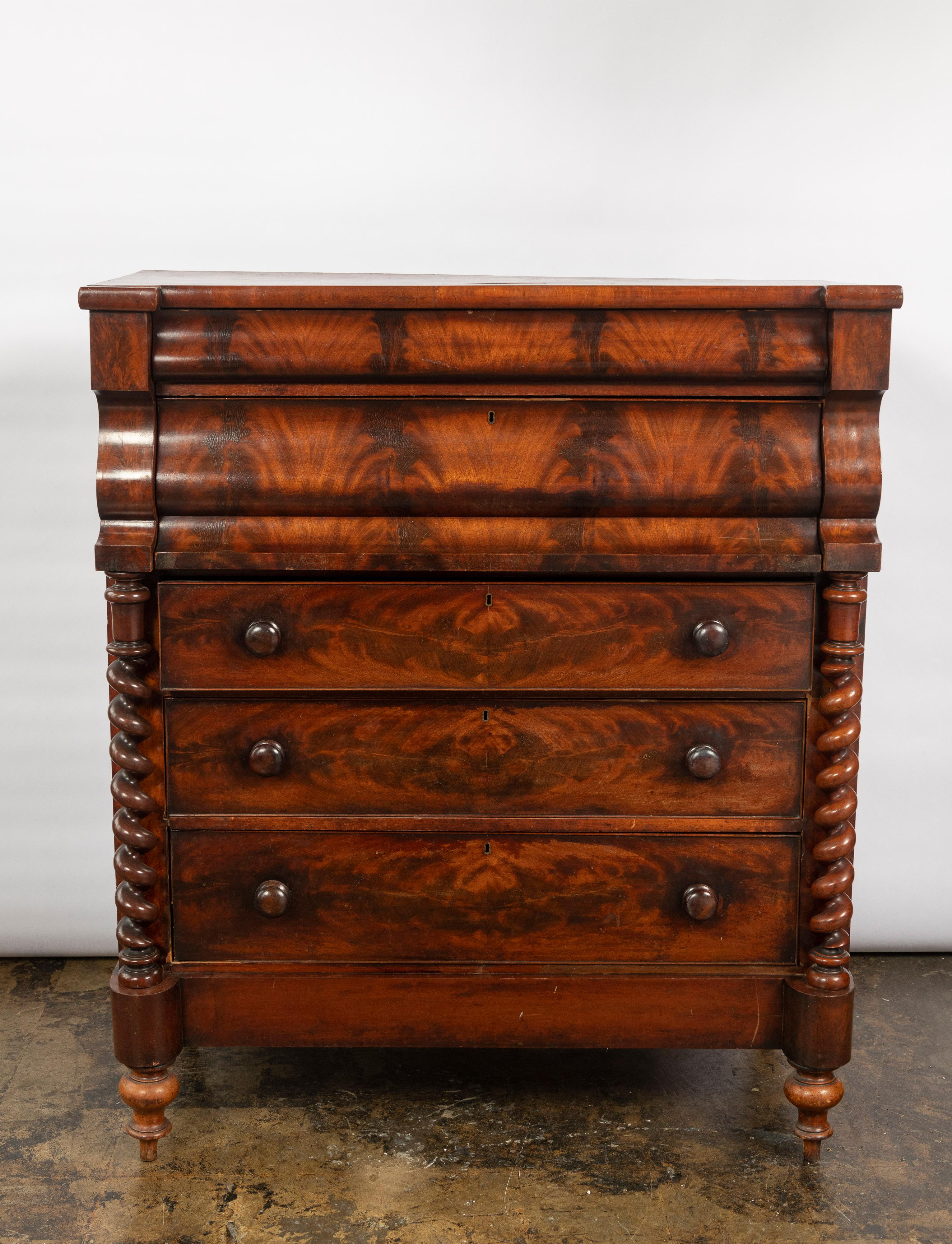 Classic tall Scottish ogee chest of drawers in good, untouched condition made of beautiful flame mahogany veneers. The five large drawers have oak sides and dovetail joints with original wooden knobs. The hand carved scrolled columns are quite