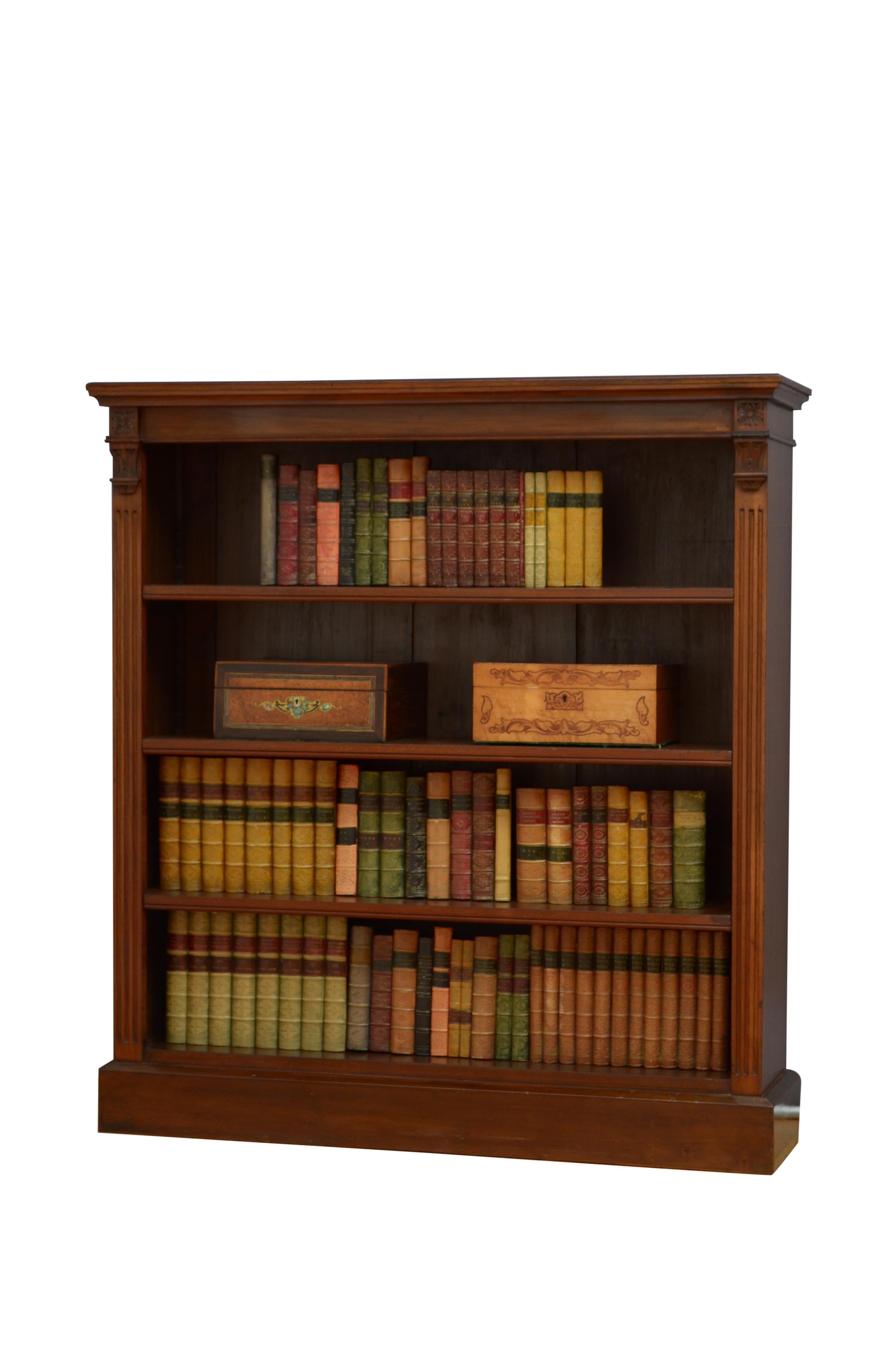 0596 Victorian open bookcase in mahogany, having figured top above shallow frieze and three height adjustable shelves, all flanked by reeded pilasters and drop carvings, standing on plinth base. This antique bookcase retains its original finish