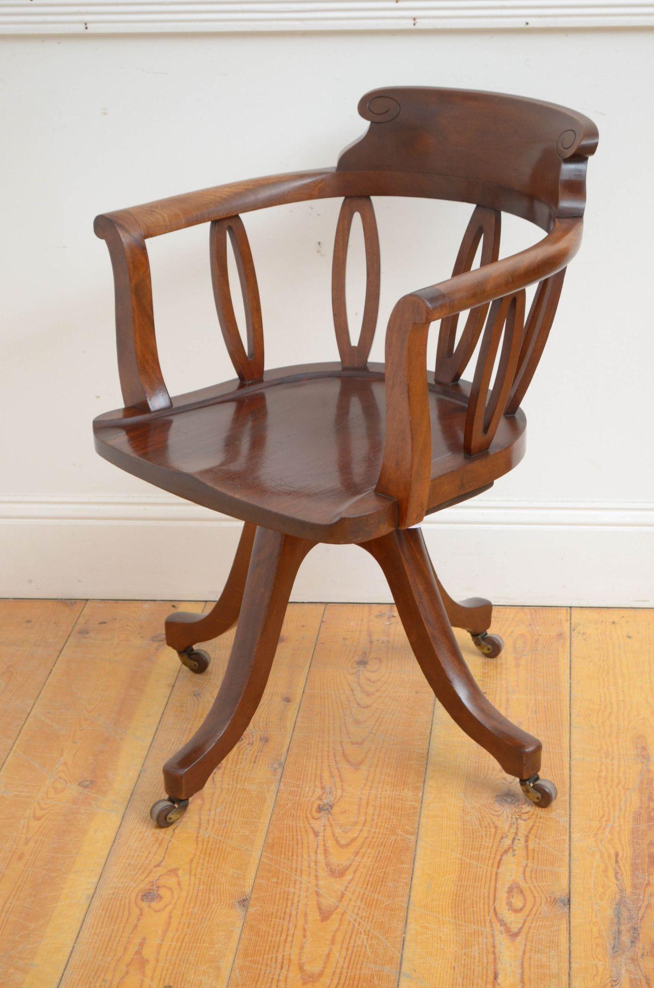 Sn5425 An English Victorian solid mahogany desk chair, having shaped top rail with carved uprights, generous seat and open scroll arms, all standing on four cabriole les terminating in brass castors. This antique chair in home ready condition.