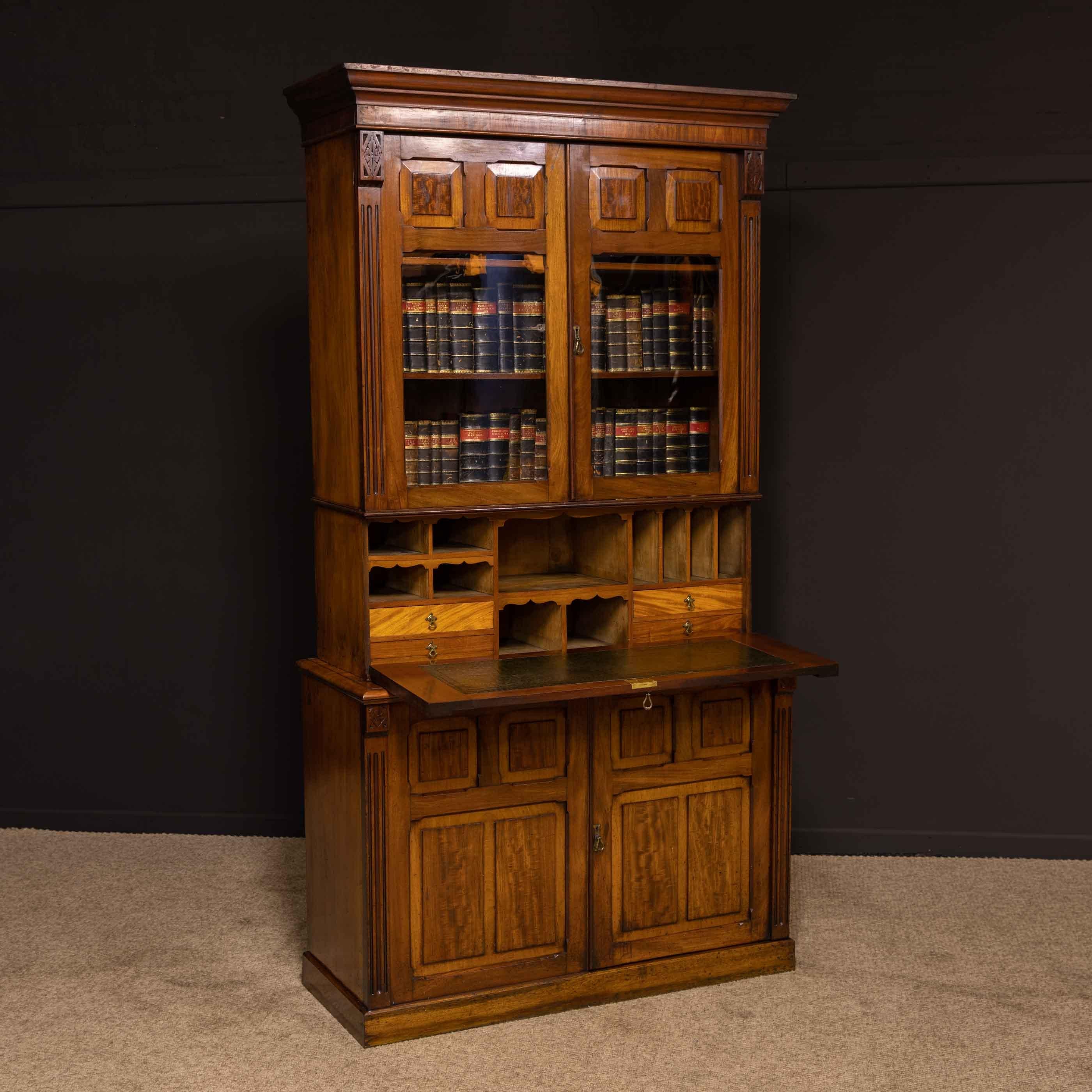 A quality, impressively sized secretaire bookcase with strong Aesthetic overtones in its design. The two cupboard base has square and rectangular panels which are carved through to the upper structure. The secretaire drops down to reveal a newly