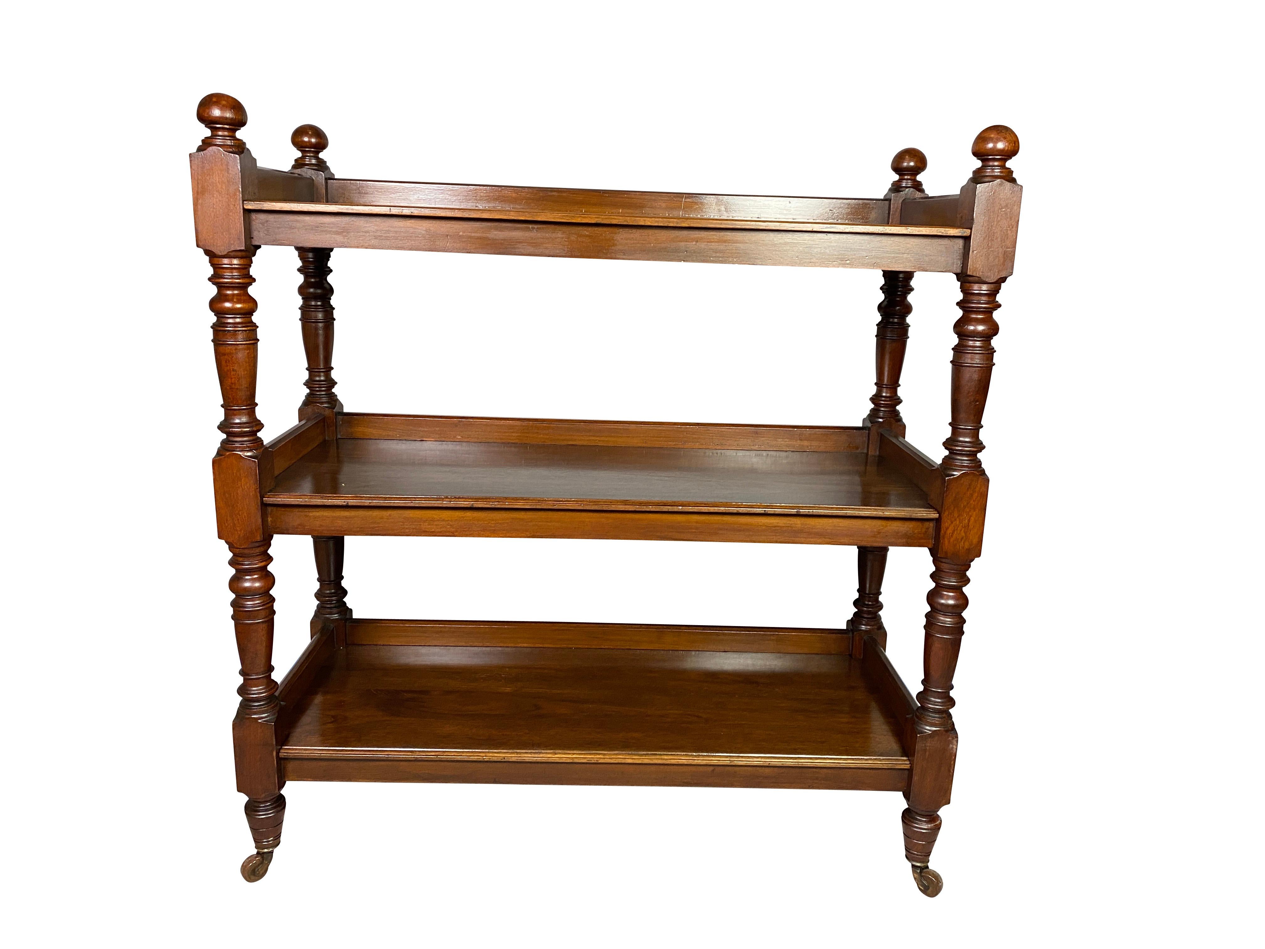 Rectangular top with corner finials over two conforming shelves all raised on turned supports, toupie feet and casters.