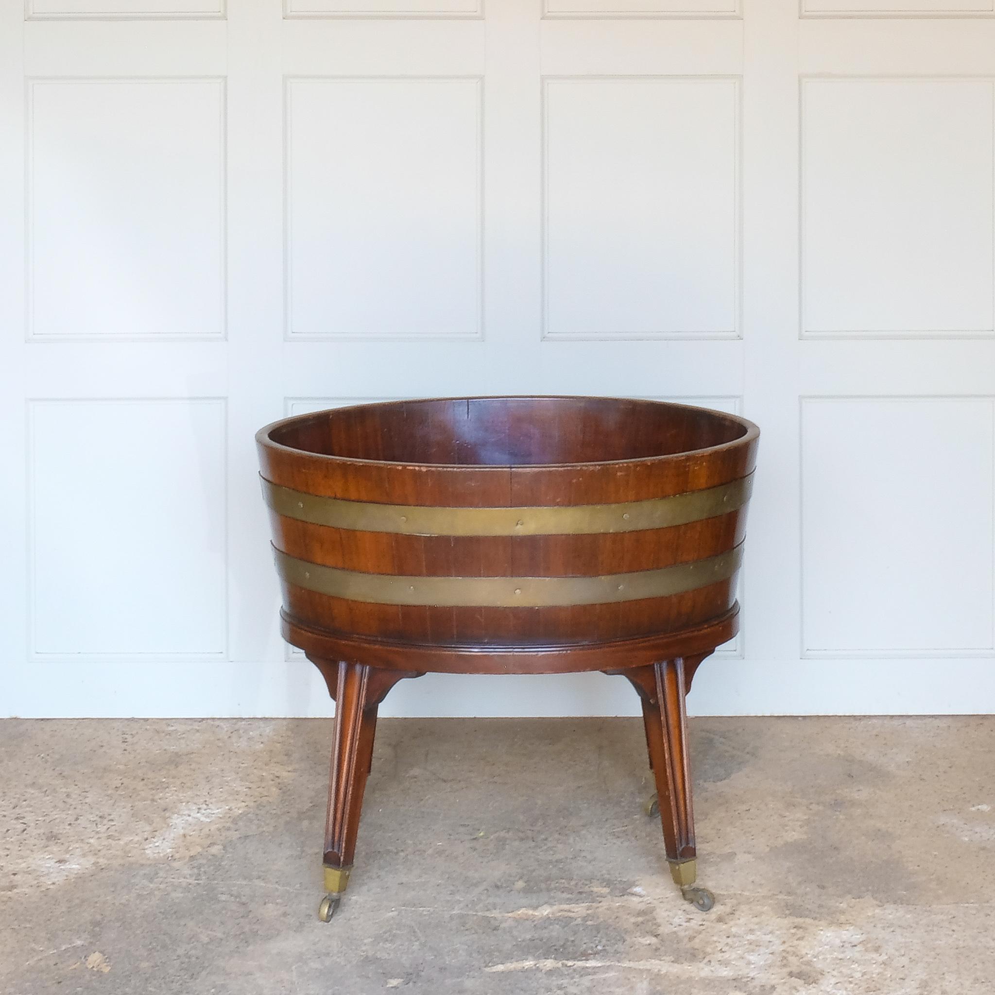 A late Victorian mahogany and brass bound wine cooler, late 19th century, in an oval form with two brass bands, on gently tapering moulded square legs with brass caps and castors, some minor age related patina commensurate with use, in good