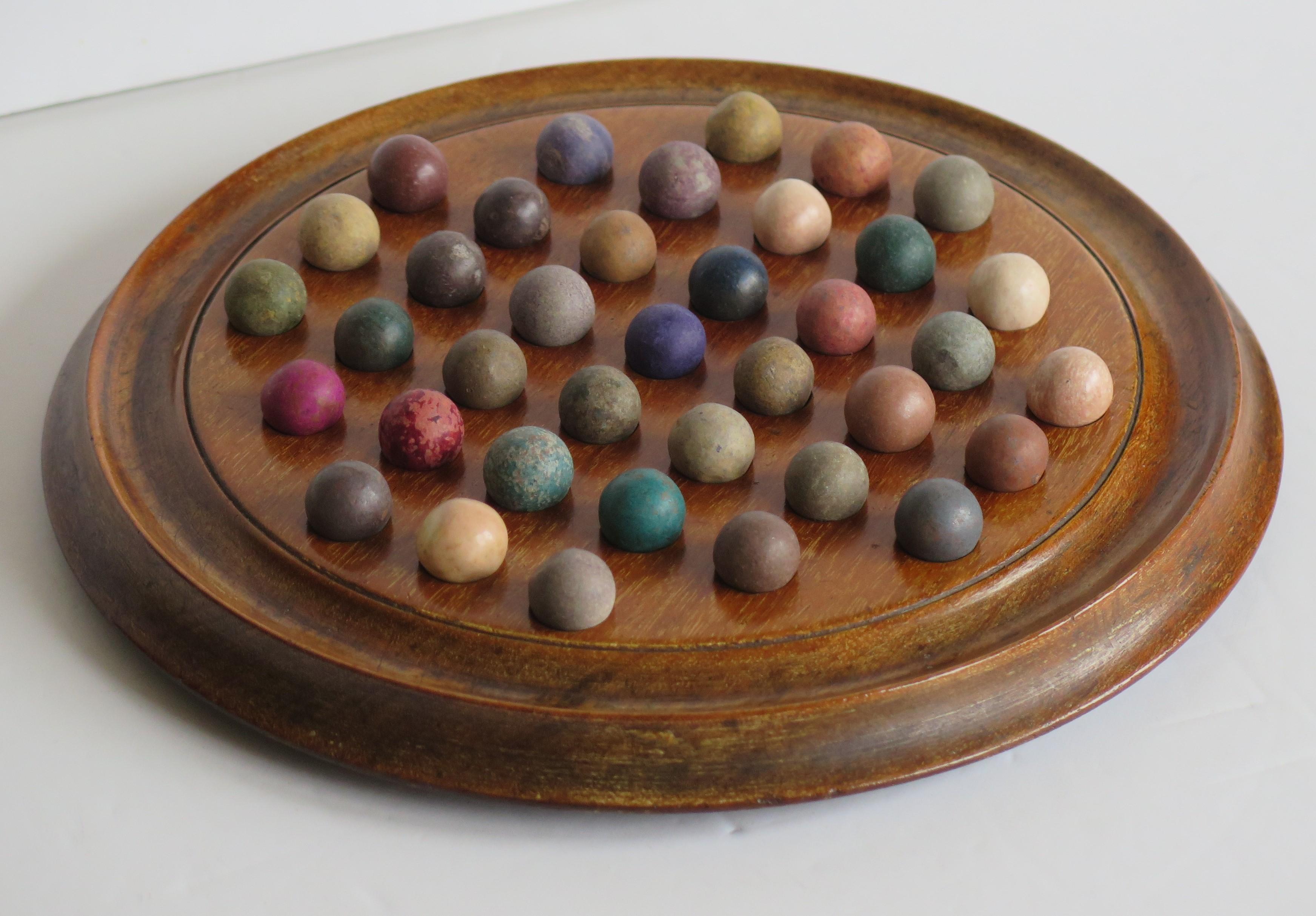 This is a complete marble solitaire game, having a beautiful hardwood board and a complete set of 37 clay or stone handmade marbles, all dating to the mid-19th century Victorian period.
 
This board is a really good example. It is circular and very