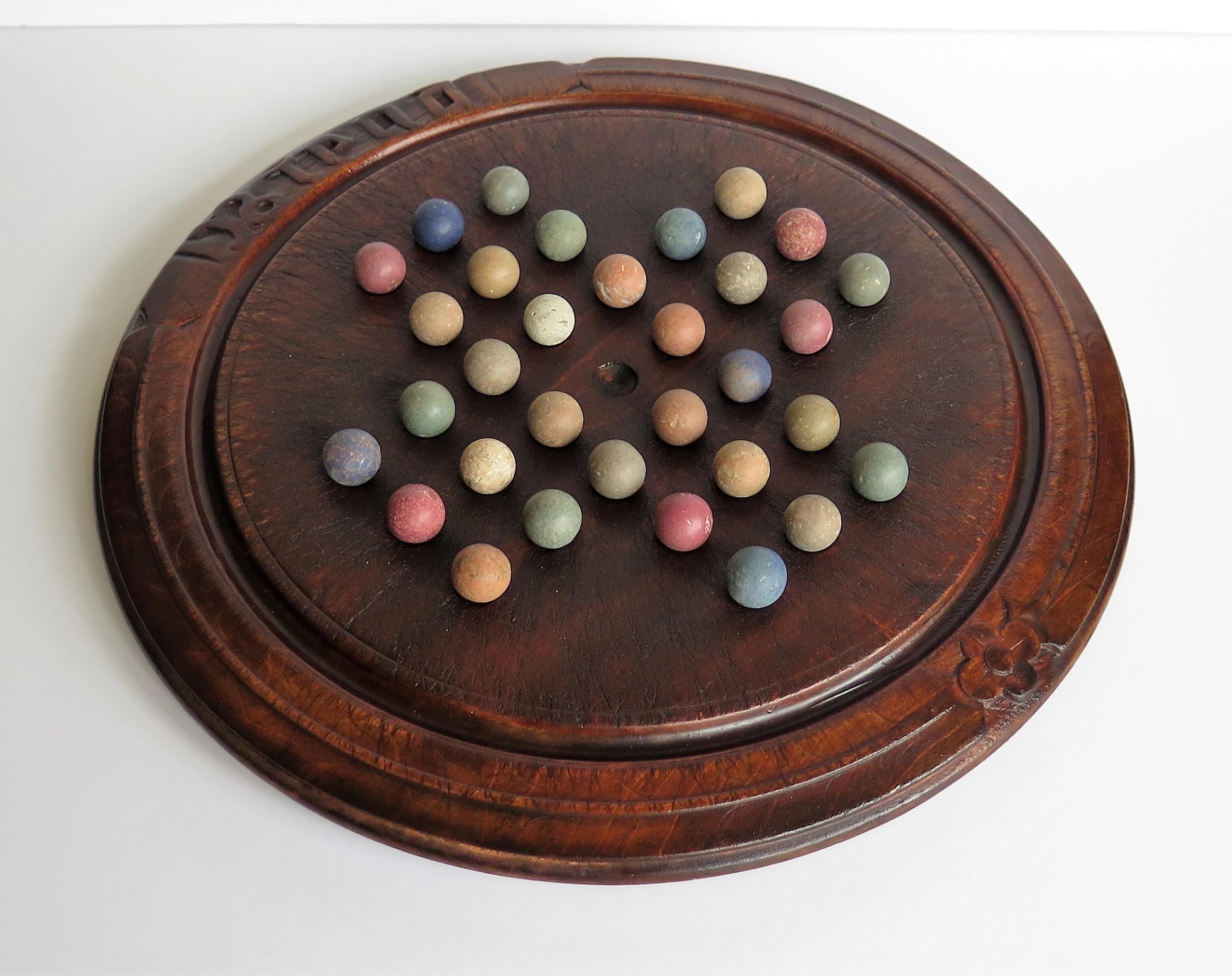 This is an unusual game of marble solitaire from the 19th century Victorian period with an old carved bread board converted to a solitaire game board with 32 early clay and stone marbles. 

This board was originally a Victorian bread board,