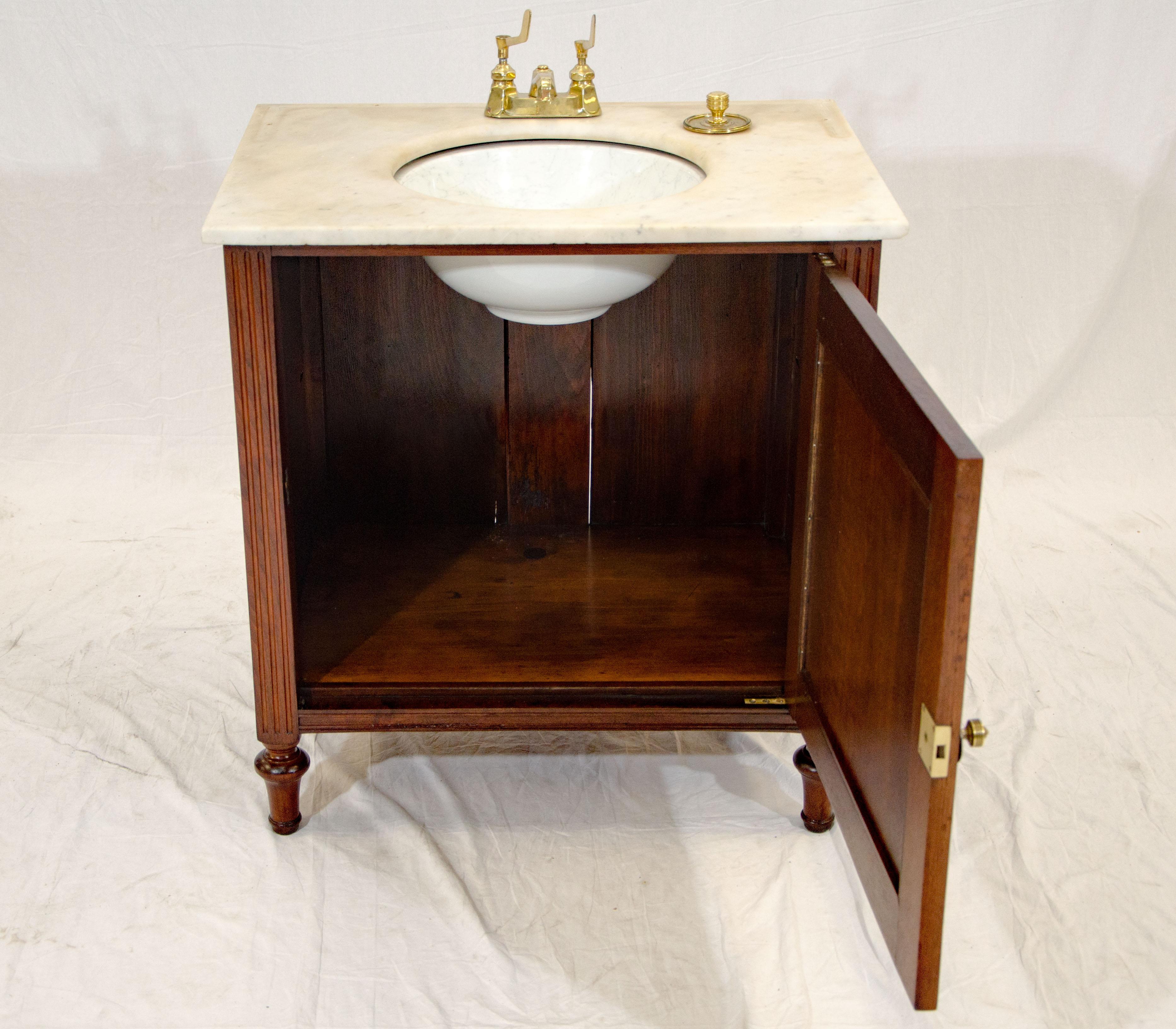 This Victorian walnut cabinet has a marble top, a circular sink, and brass fixtures. There is evidence of a marble backsplash being attached at one time. You can customize the sink with marble or waterproof wooden gallery backsplash. The brass