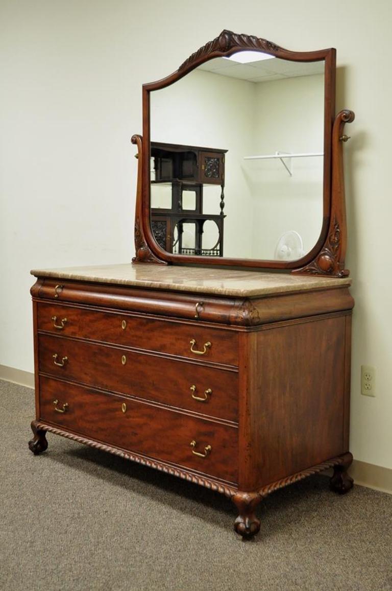 Antique marble-top solid carved mahogany Victorian low dresser and matching mirror. Item features carved ball and claw feet, acanthus and medallion accented harps and mirror frame, four dovetail constructed drawers, rich natural wood grain, and