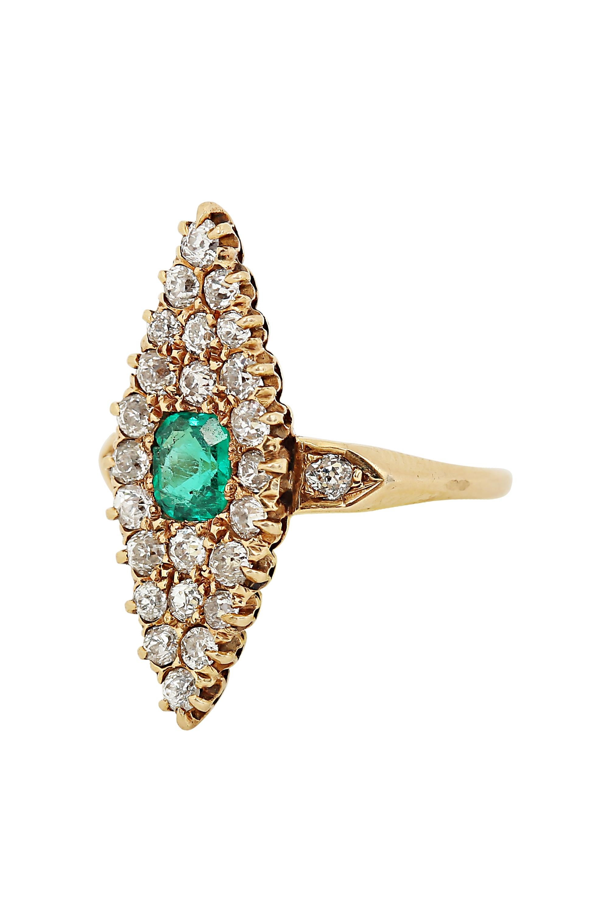 This refined and lovely Victorian ring spotlights a vibrant octagon shaped emerald within a navette shaped field of glittering mine cut diamonds, subtly enhanced at the shoulders with two single diamonds. Set with approximately 1.60 carats of