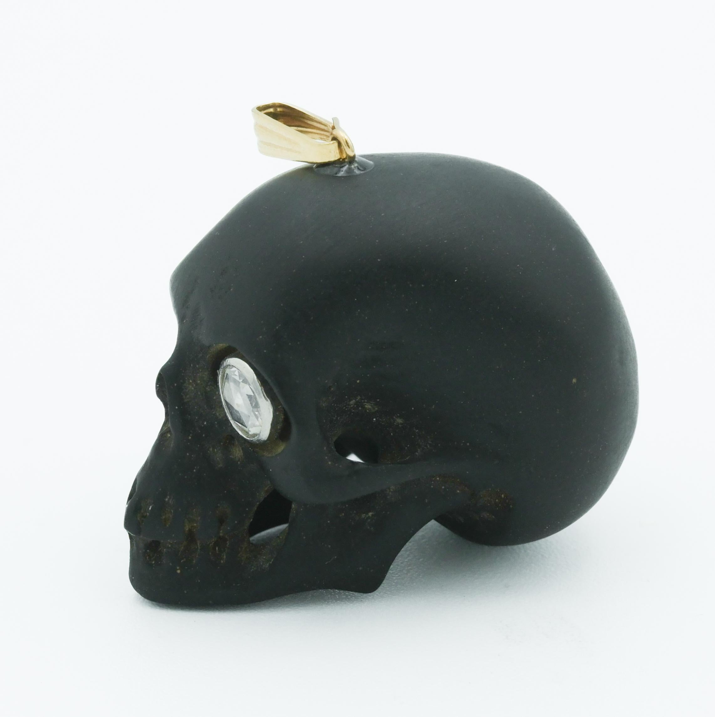 This striking vintage skull pendant is a captivating piece of jewelry that blends gothic charm with classic elegance. The pendant is skillfully carved from what appears to be jet or charcoal, providing a deep, matte contrast to the gleaming