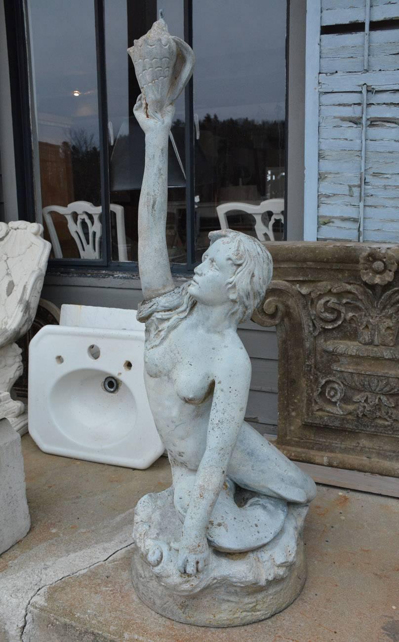 The Victorian garden fountain is of a mermaid sitting on shore-line rocks. The arm stretches upward as she holds a conch shell which is the base for the fountain. Water flows from the pipe placed in the upper tip of the shell. The fountain is made