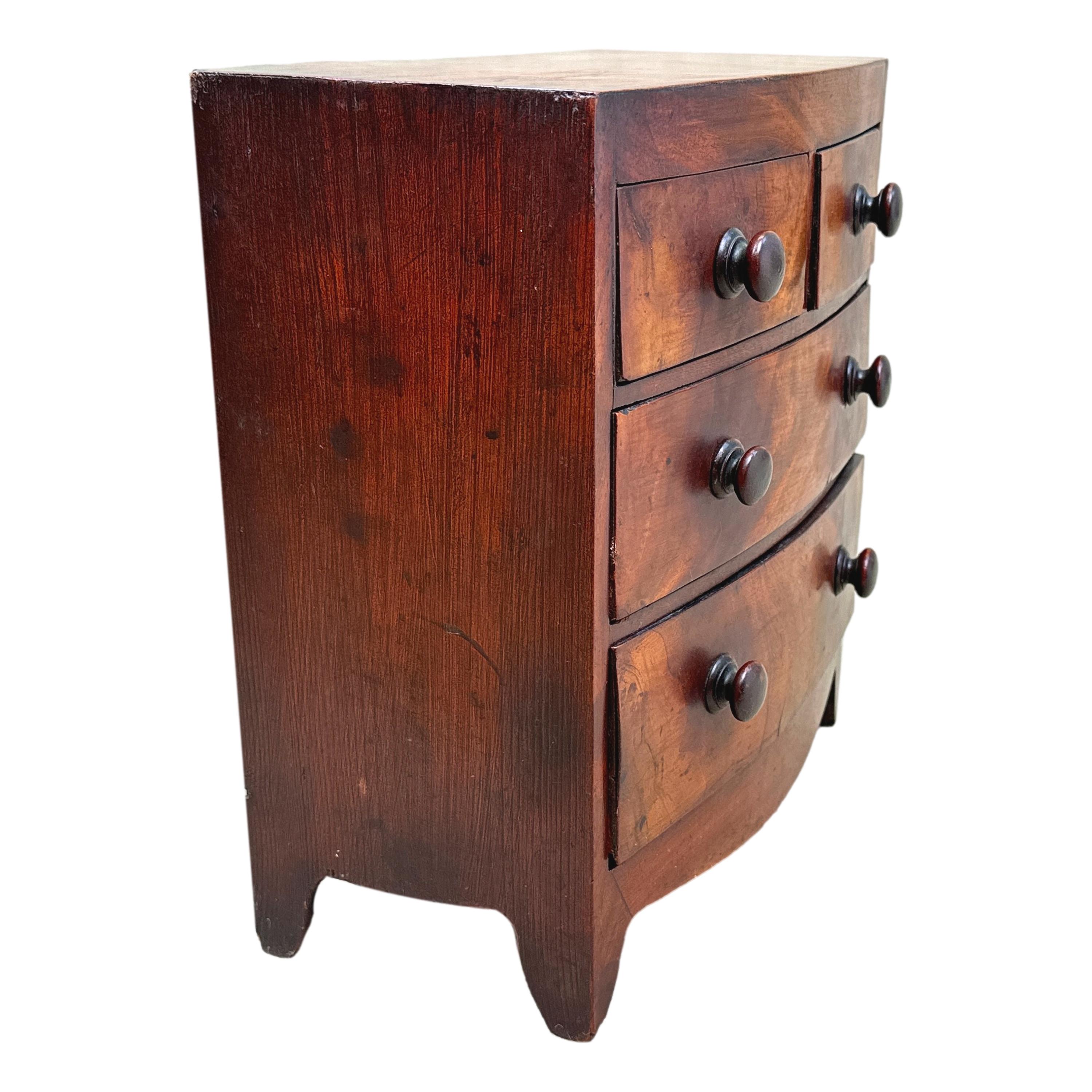 An Attractive And Elegant Mid 19th Century, Victorian Period, Mahogany Bowfront Miniature Mahogany Chest, Having Very Well Figured Top, Over Two Short And Two Long Drawers Retaining Original Turned Knobs, Raised On Elegant Original Splayed Bracket