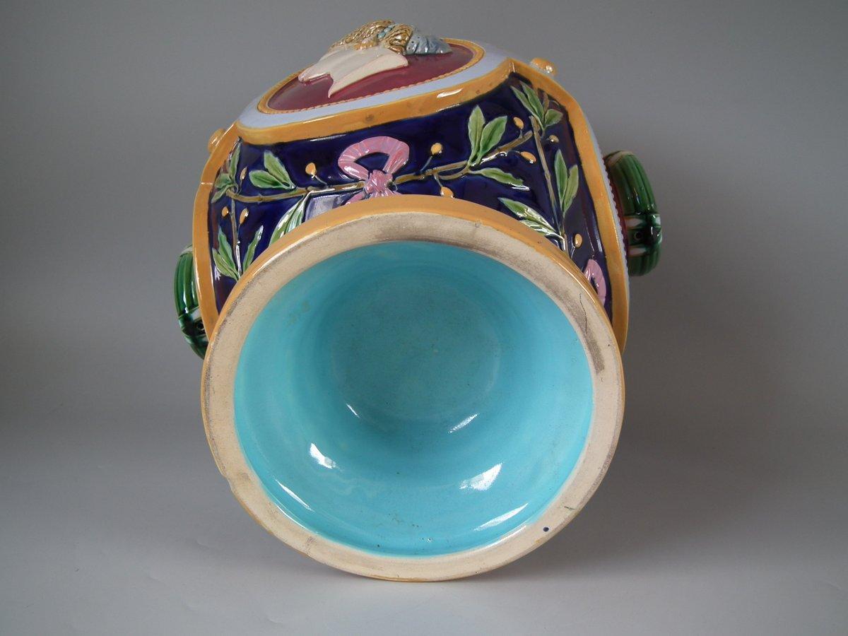 Minton Majolica jardinière which features four relief molded panels around the body, two with a female head in profile representing 'The Americas' and 'Africa', the other two with ring handles bound with green ribbon. Coloration: ochre, cobalt blue,
