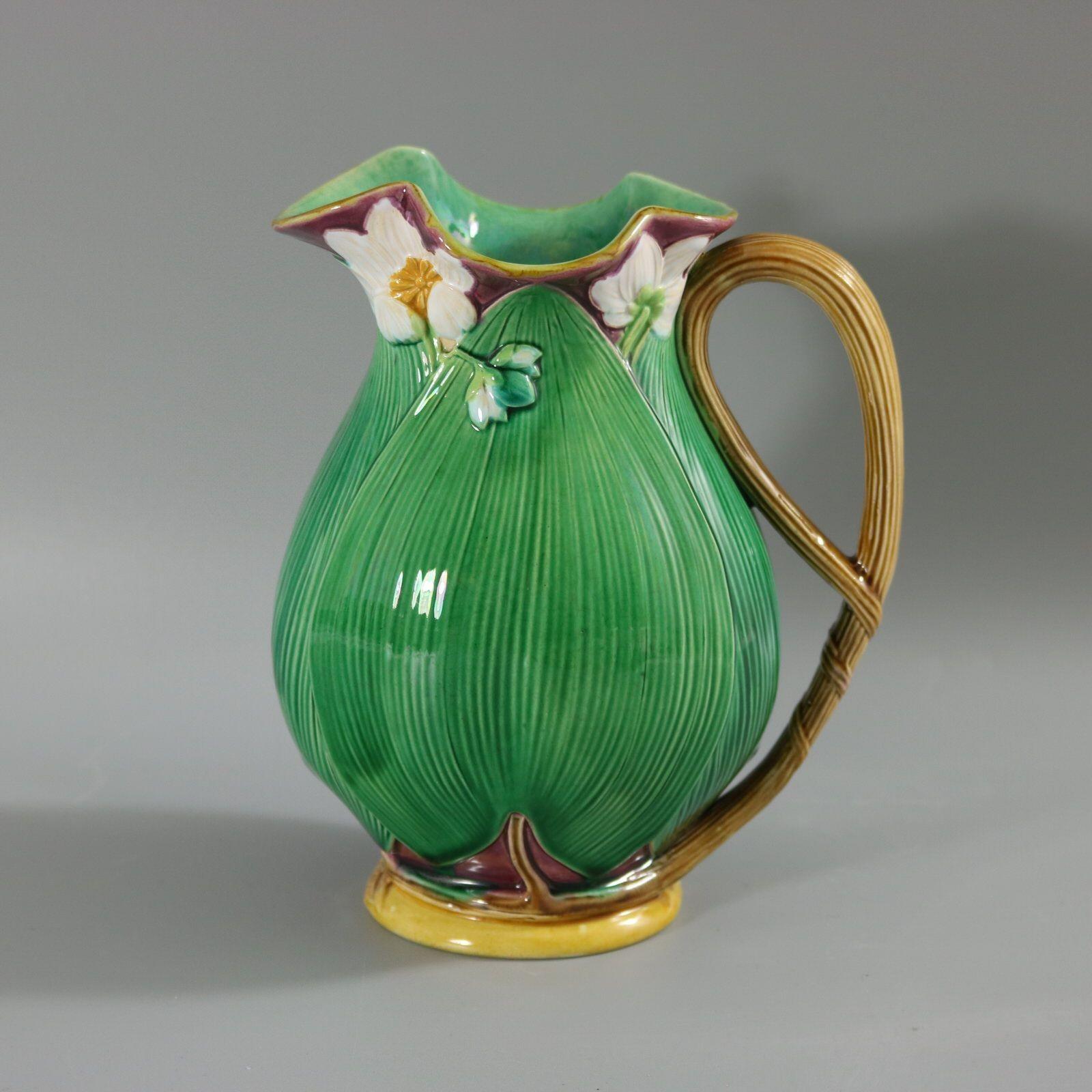 Minton Majolica jug/pitcher which features flowering lilies and lily pads. Colouration: green, white, dark pink, are predominant. The piece bears maker's marks for the Minton pottery. Bears a pattern number, '1228 18'. Marks include a factory