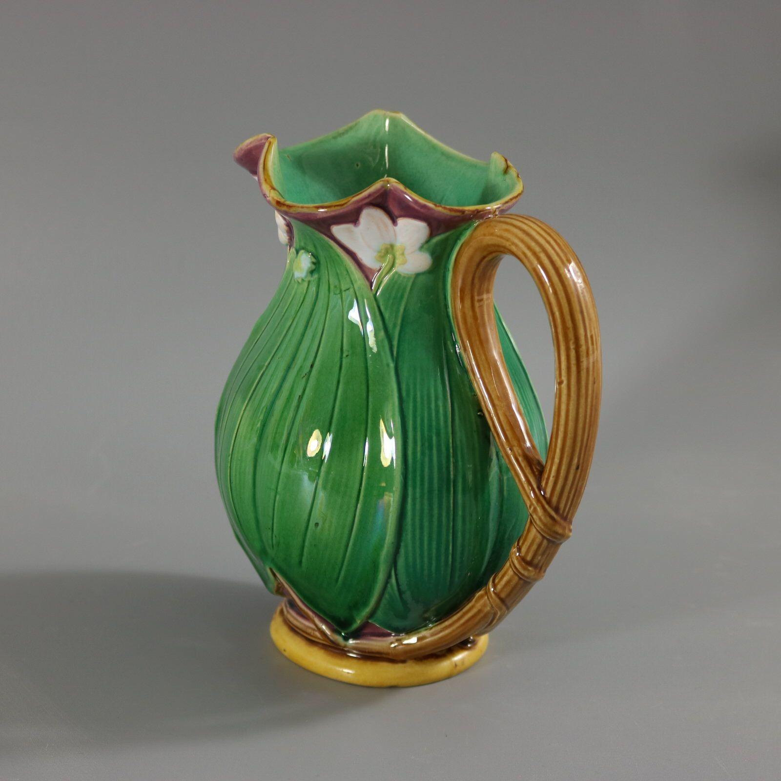 Minton Majolica jug/pitcher which features flowering lilies and lily pads. Colouration: green, white, dark pink, are predominant. The piece bears maker's marks for the Minton pottery. Bears a pattern number, '1228'.