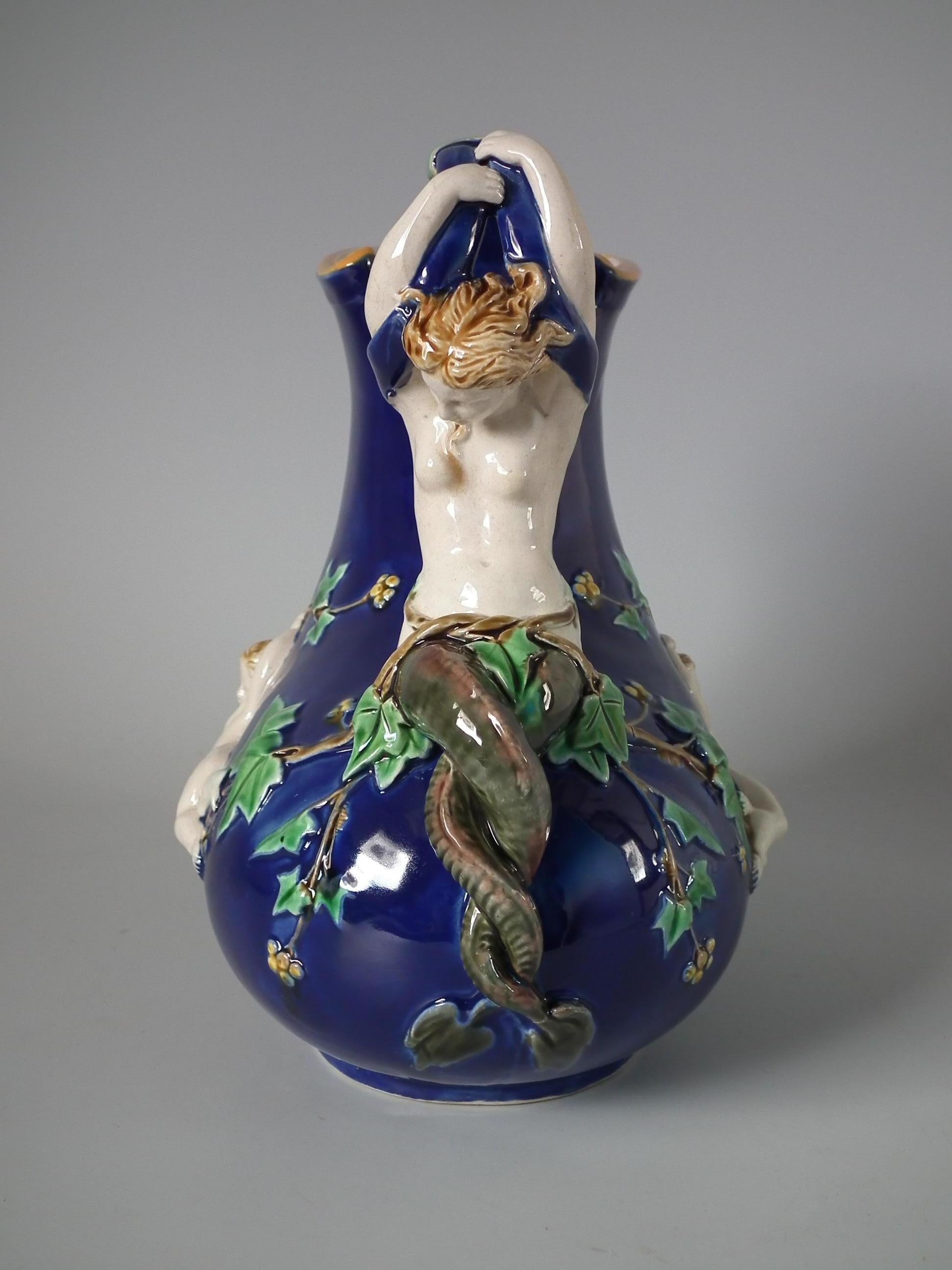 Minton Majolica jug/pitcher which features a handle in the form of a mermaid with entwined tail, a satyr mask below the spout and cherubs hanging from grape vines across the sides. Cobalt blue ground version. Colouration: cobalt blue, green, white,