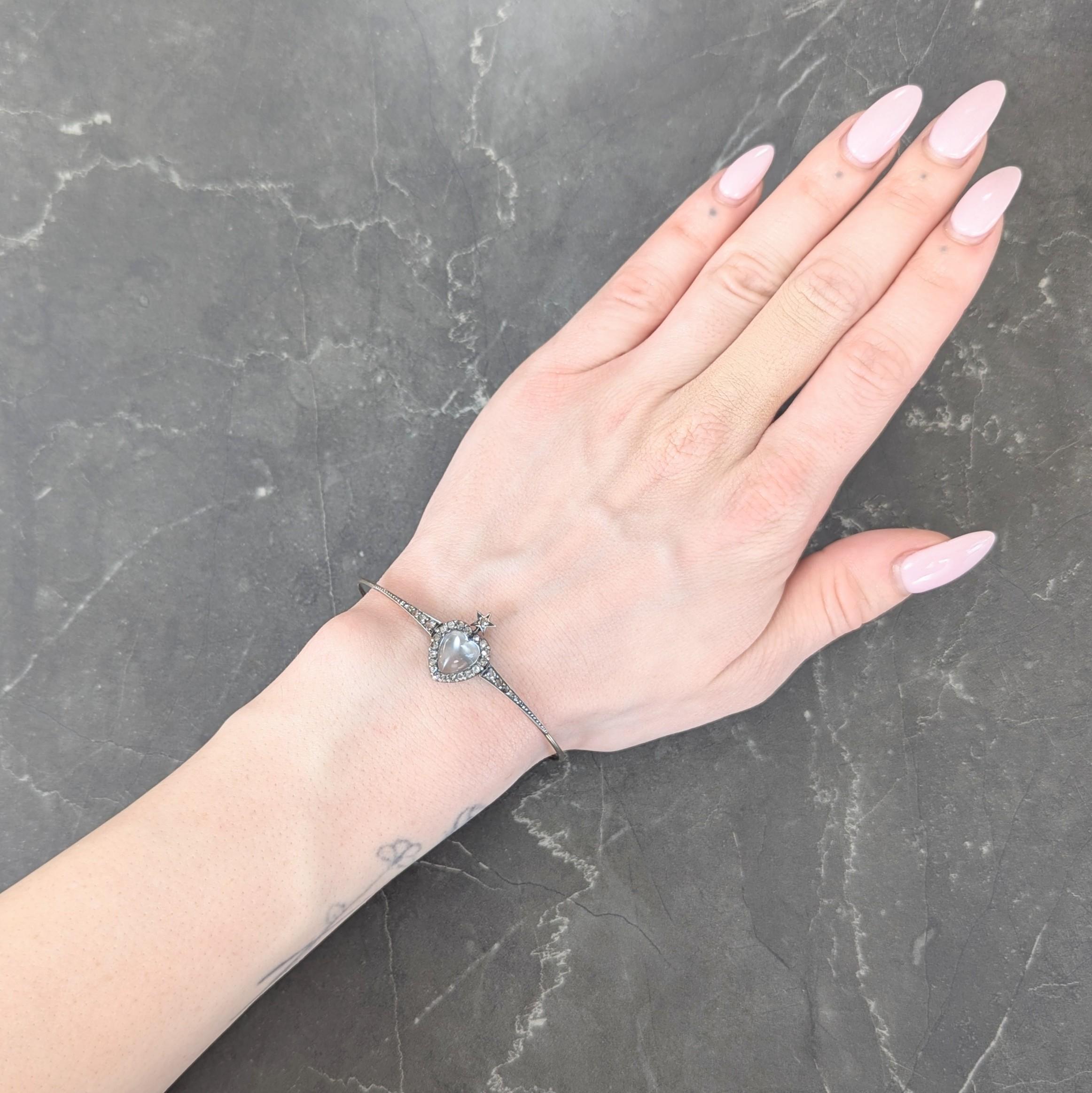 Designed as an expanding gold bangle bracelet centering a silver-topped station
Featuring a heart shaped moonstone measuring 8.5 x 9.5 mm - prong set
Colorless body with white adularescence - accented by halo surround
Adorned with star motif and