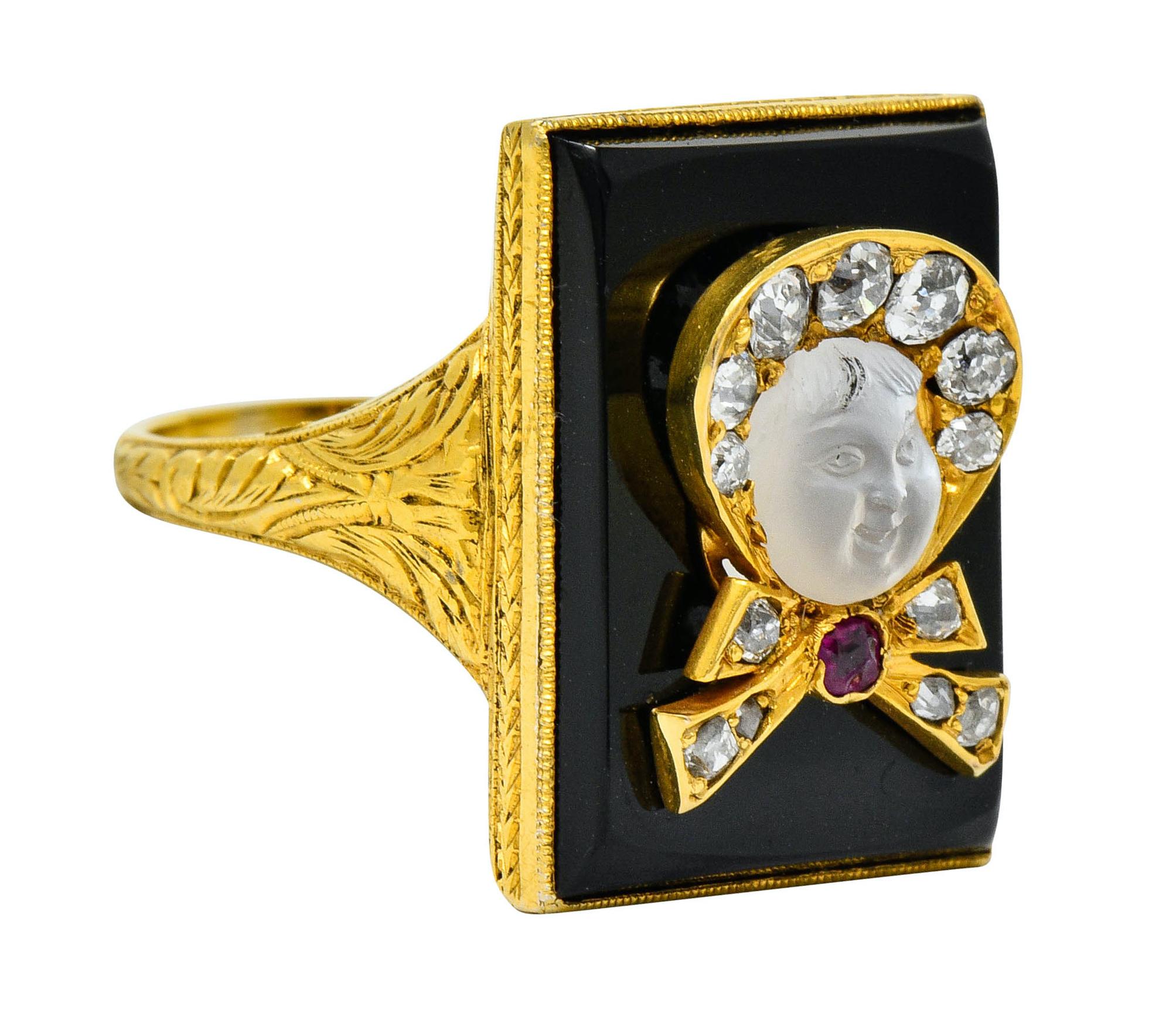 Rectangular statement ring designed as an ornately engraved mounting featuring a bezel set tablet of onyx with excellent polish

Centering a dimensional depiction of a baby in a bowed bonnet accented by a cushion cut ruby

Face is a deeply carved